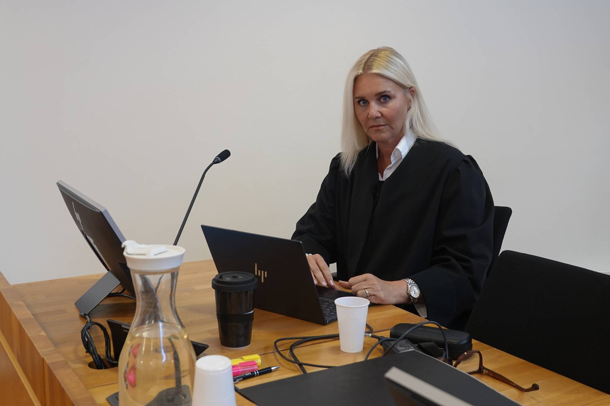 En kvinne i dommerdrakt sitter ved et skrivebord med en bærbar datamaskin. (Bildebeskrivelsen er laget av en KI-tjeneste)