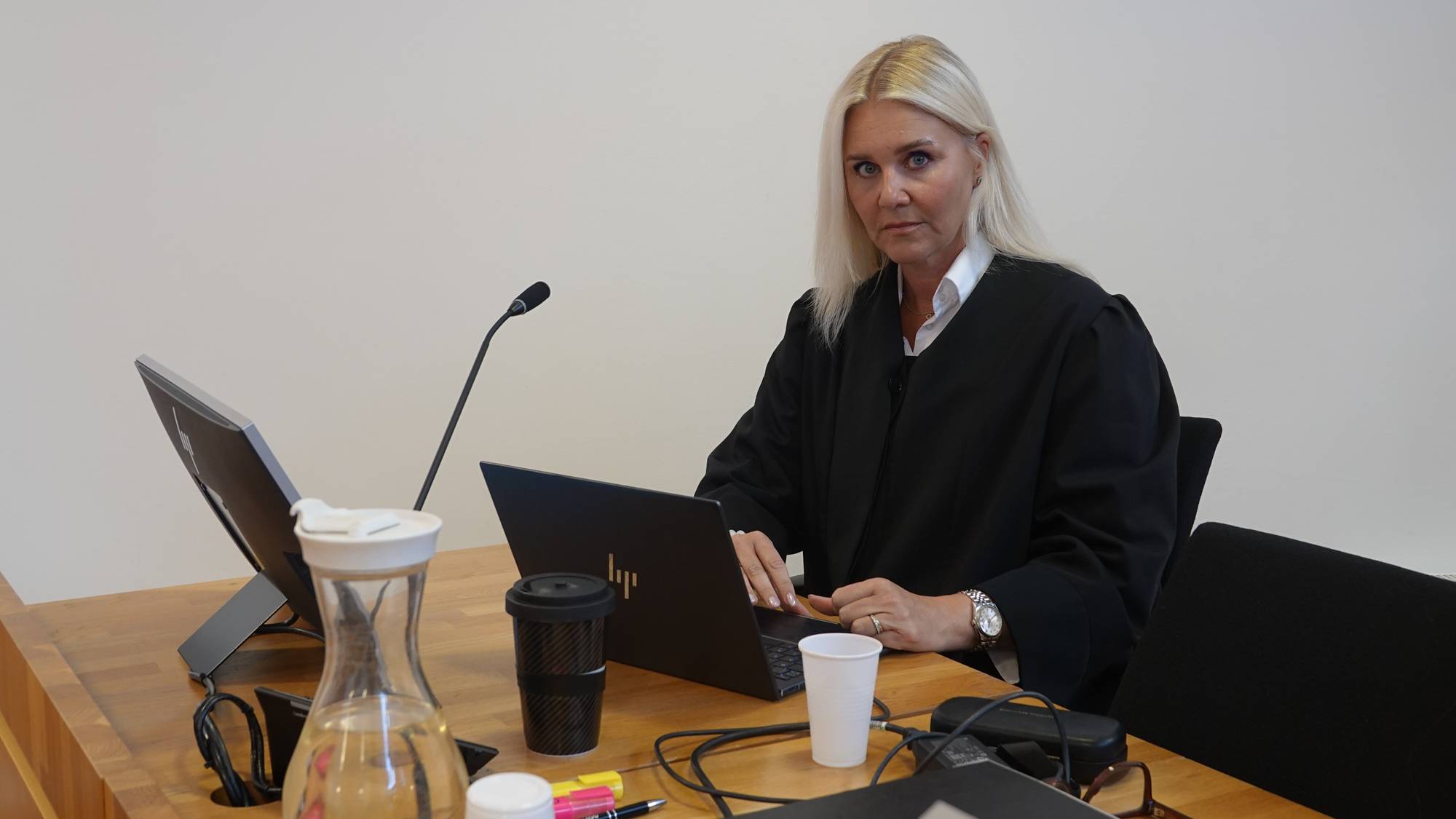 En kvinne i dommerdrakt sitter ved et skrivebord med en bærbar datamaskin. (Bildebeskrivelsen er laget av en KI-tjeneste)