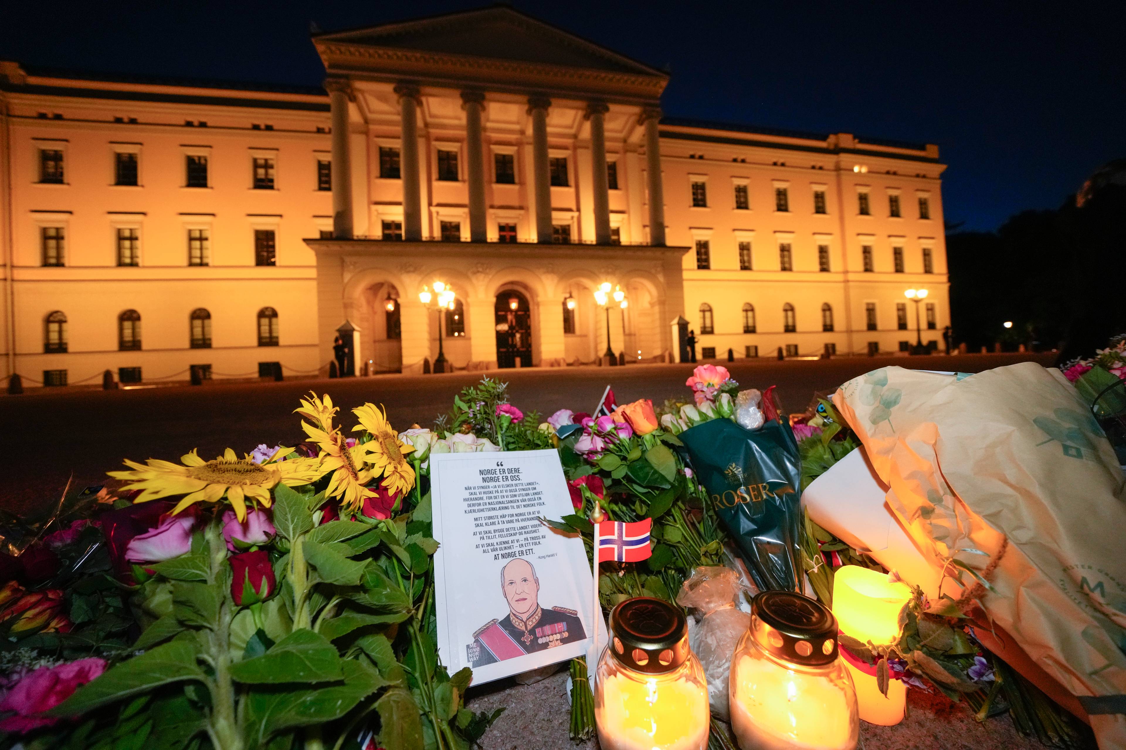 Blomster og tente lys foran Det kongelige slott i Oslo. En illustrasjon med kong Harald er lagt ned.