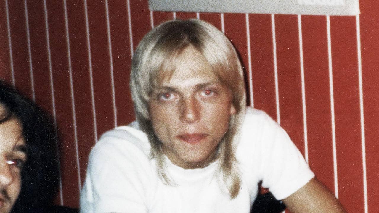 Kjetil Manheim som tenåring foran en rød yttervegg, med halv-langt blondt hår.
