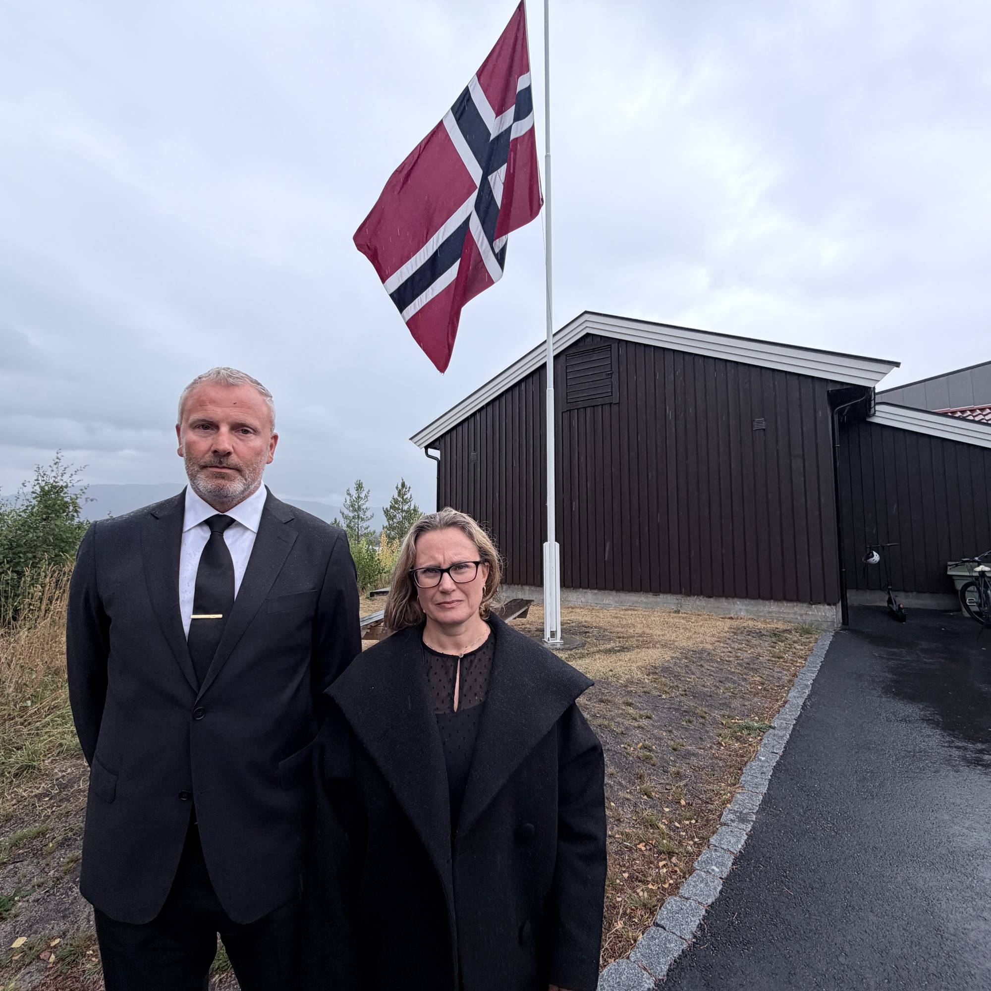 En mann og en kvinne som står foran et flagg (Bildebeskrivelsen er laget av en KI-tjeneste)
