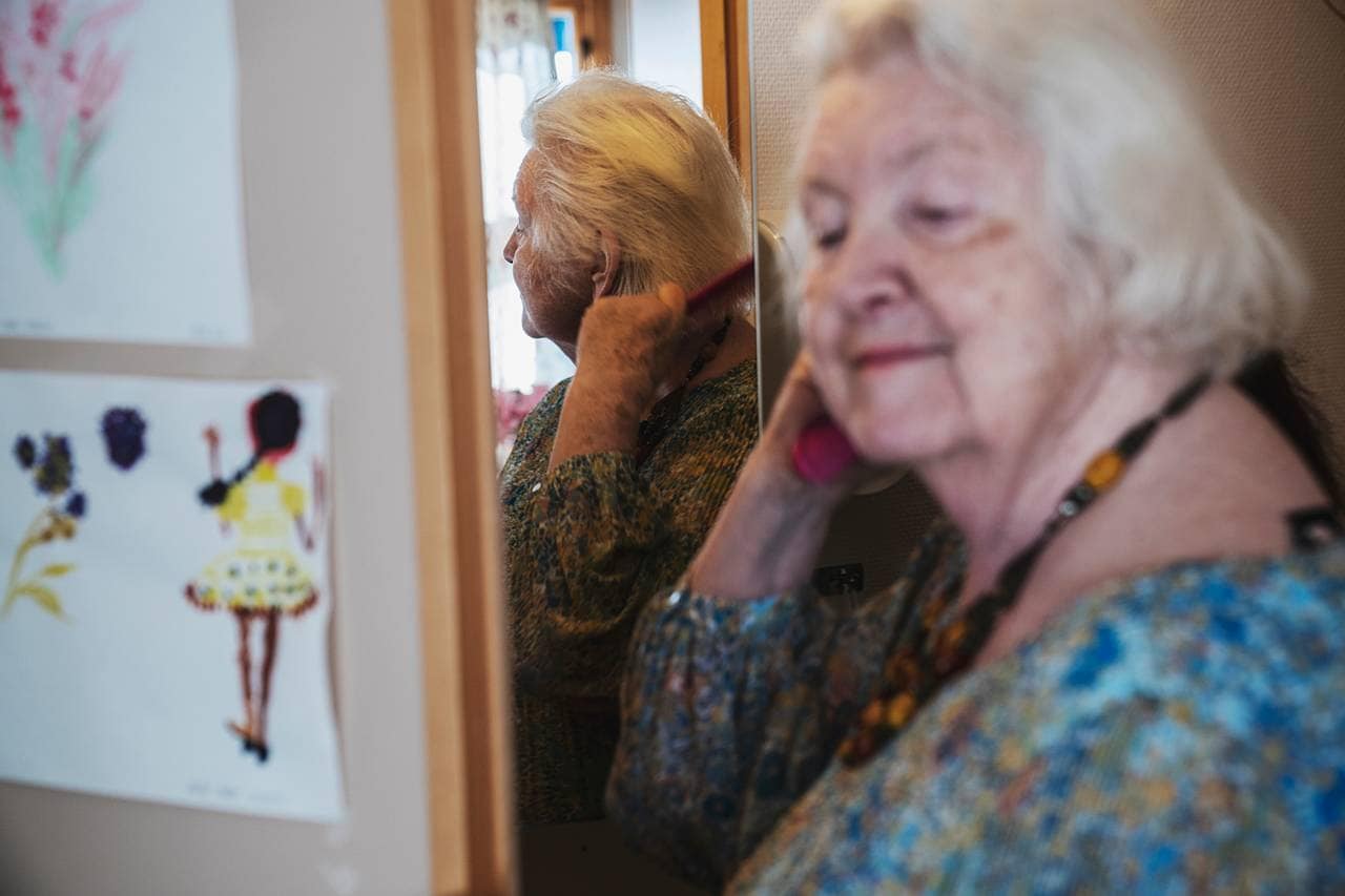 Anne Marie grer håret sitt mens hun ser seg i speilet. På veggen ved siden av henger noen tegninger hun har tegnet.