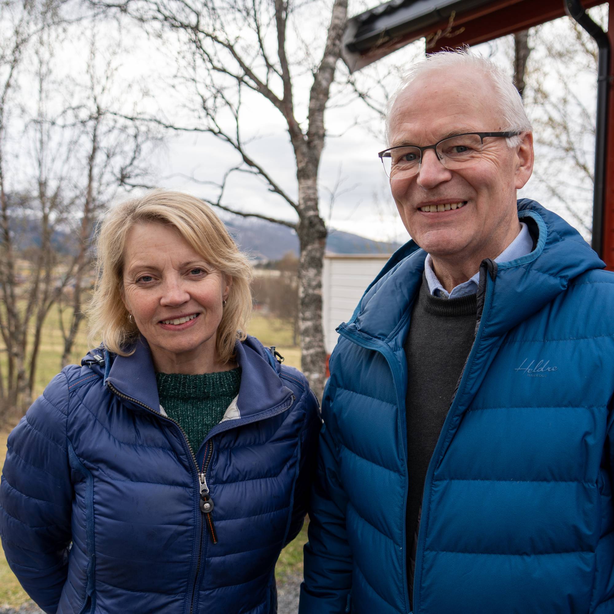 En mann og en dame står foran et hus. Begge har på blå boblejakke.