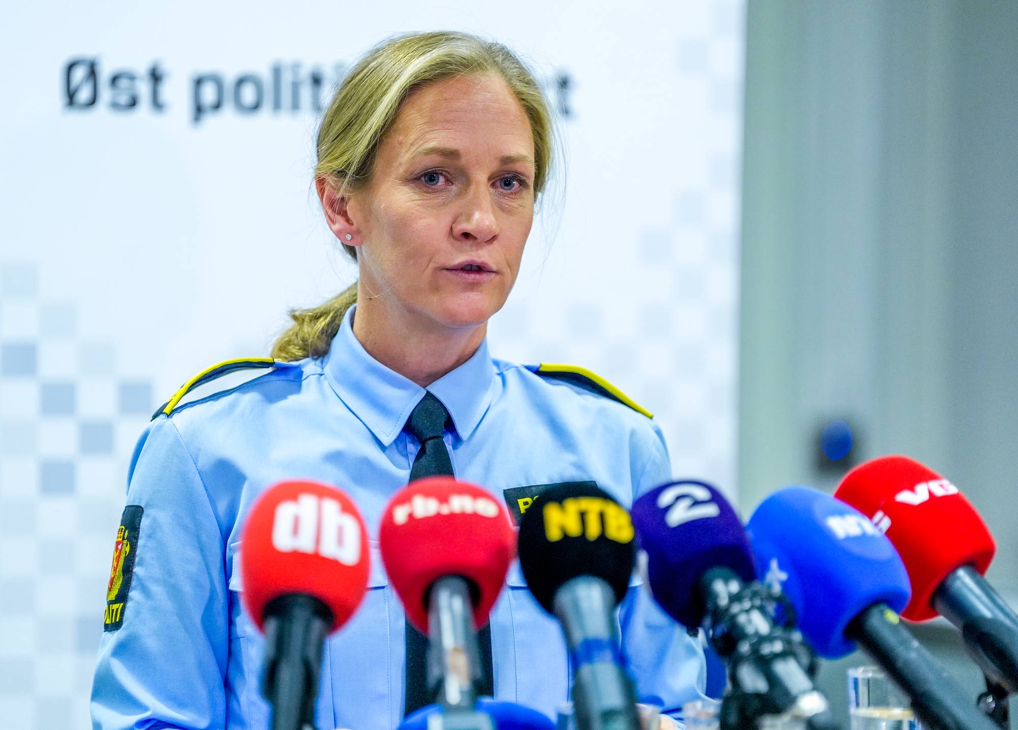 En kvinne i politiuniform snakker foran flere mikrofoner. Bak henne er det en hvit vegg med teksten "Øst politi". Hun har blondt hår i hestehale og ser mot siden. (Bildebeskrivelsen er laget av en KI-tjeneste)