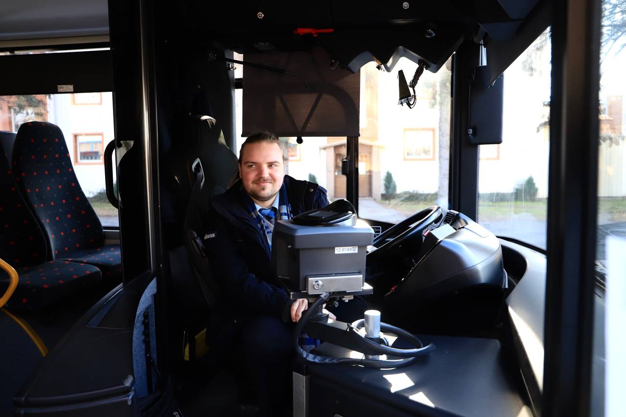 Sjåfør Simen Solbakken Johansen i Unibuss sitter bak rattet og smiler.