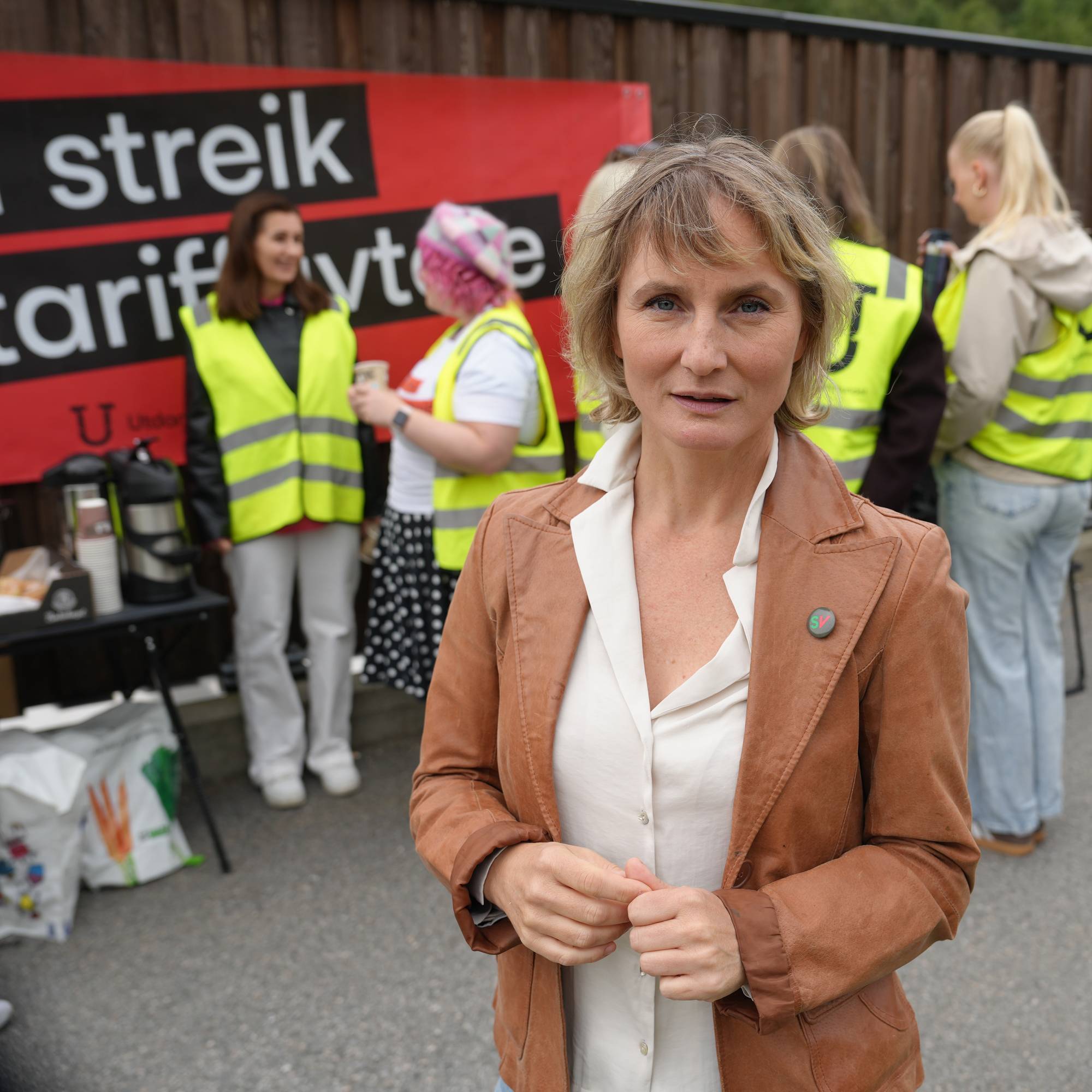 kvinne i brun jakke framfor gruppe i refleksvest