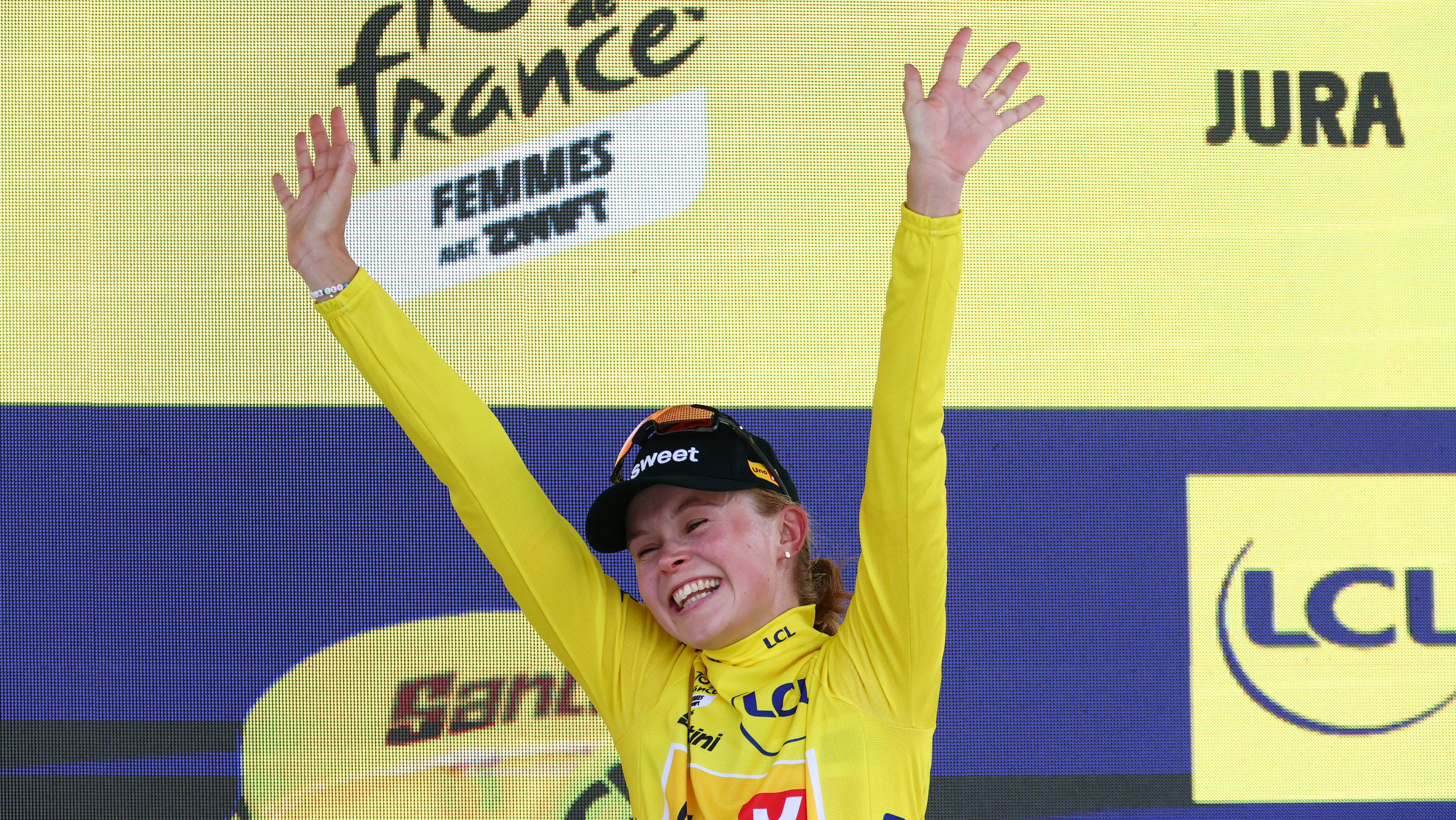 Syklist i gul ledertrøye jubler med hendene i været på seierspallen under Tour de France Femmes. (Bildebeskrivelsen er laget av en KI-tjeneste)