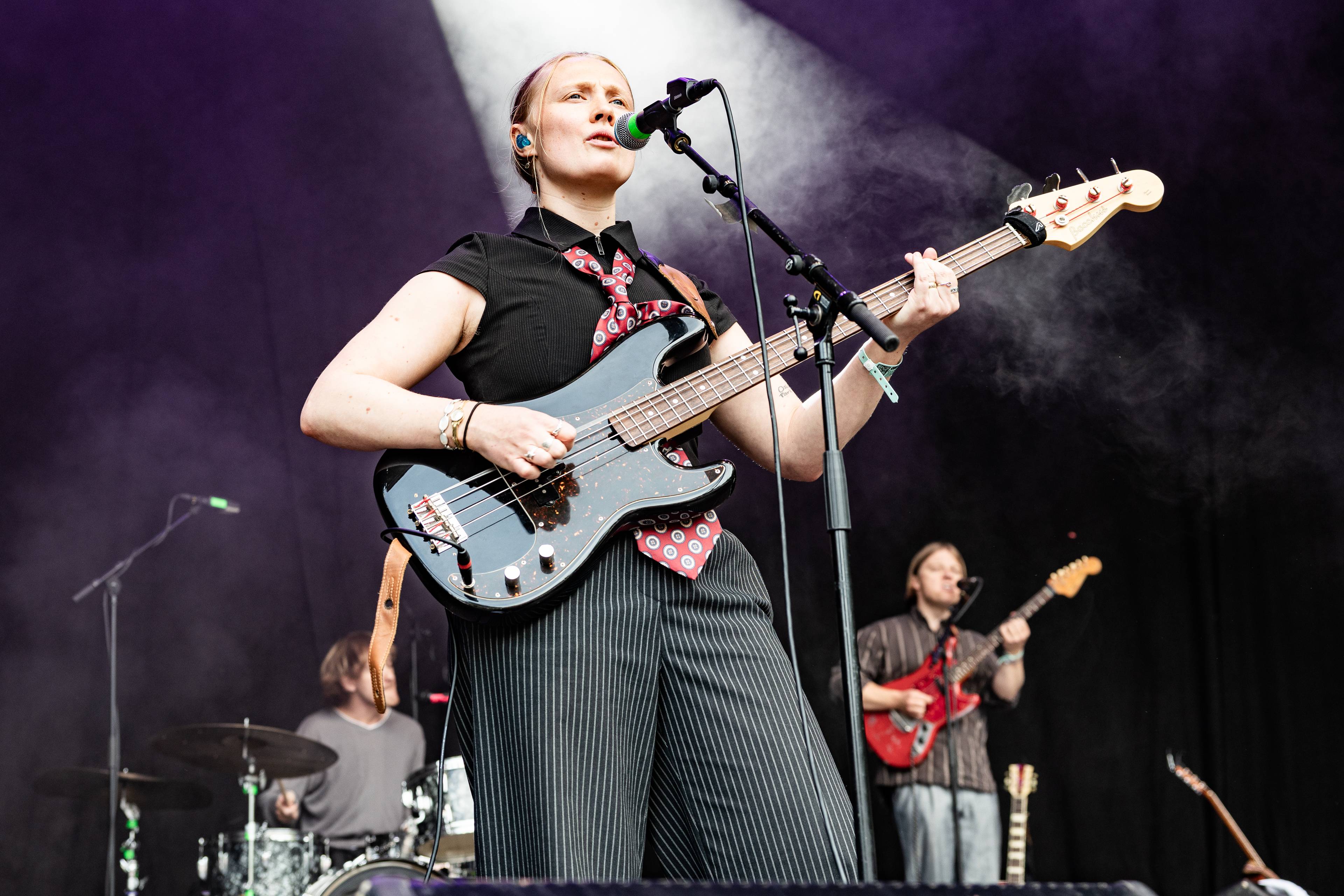 En kvinnelig musiker spiller bass og synger foran et band på en konsertscene.
