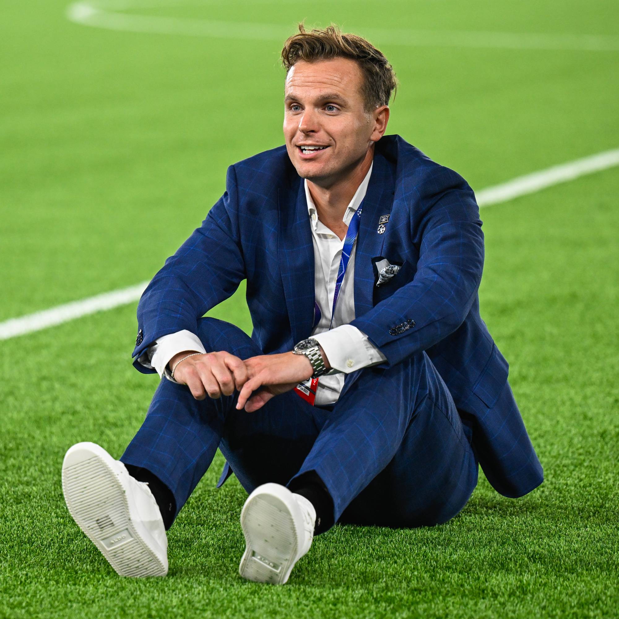 En mann i dress sitter på en fotballbane. (Bildebeskrivelsen er laget av en KI-tjeneste)