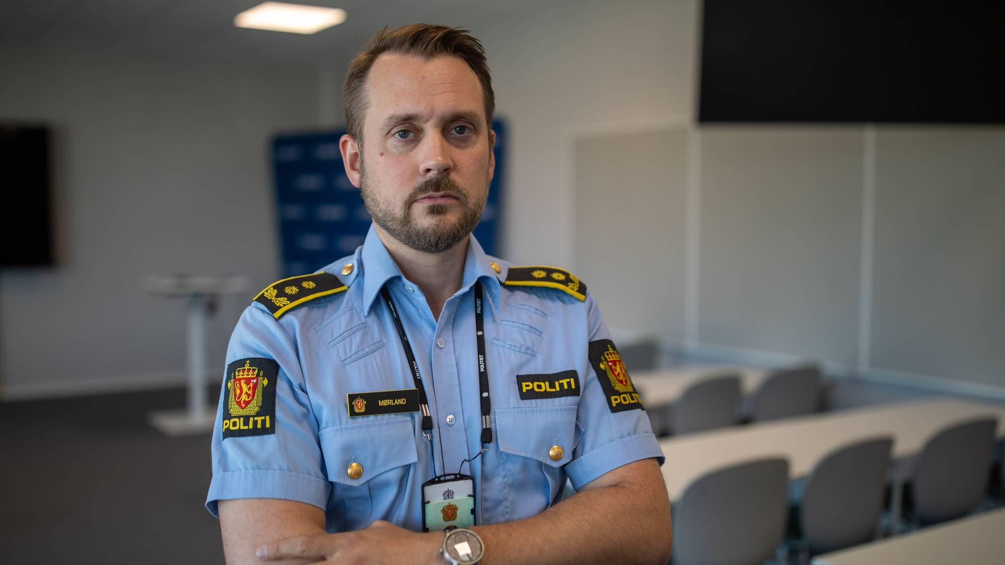 Politimann i uniform med korslagte armer i et møterom. (Bildebeskrivelsen er laget av en KI-tjeneste)