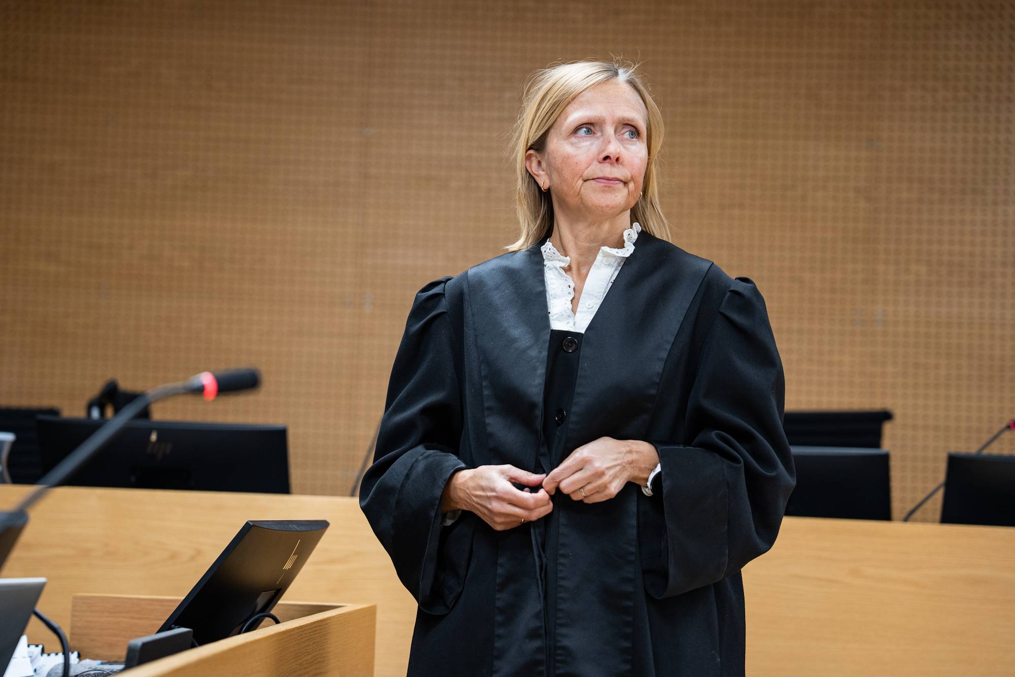 Kvinne i rettssalskjole ser bort fra kamera. Hun står i et rettslokale. Bak henne er det et paneldekt rom. Bildet er tatt fra brystet og opp. (Bildebeskrivelsen er laget av en KI-tjeneste)