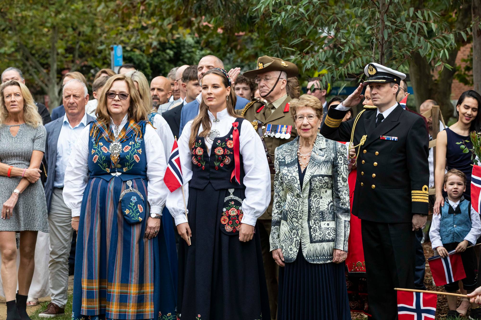 Prinsesse Ingrid Alexandra i sort bunad med broderier og hvit bluse med søljer, foran i en flokk med voksne, pyntede mennesker