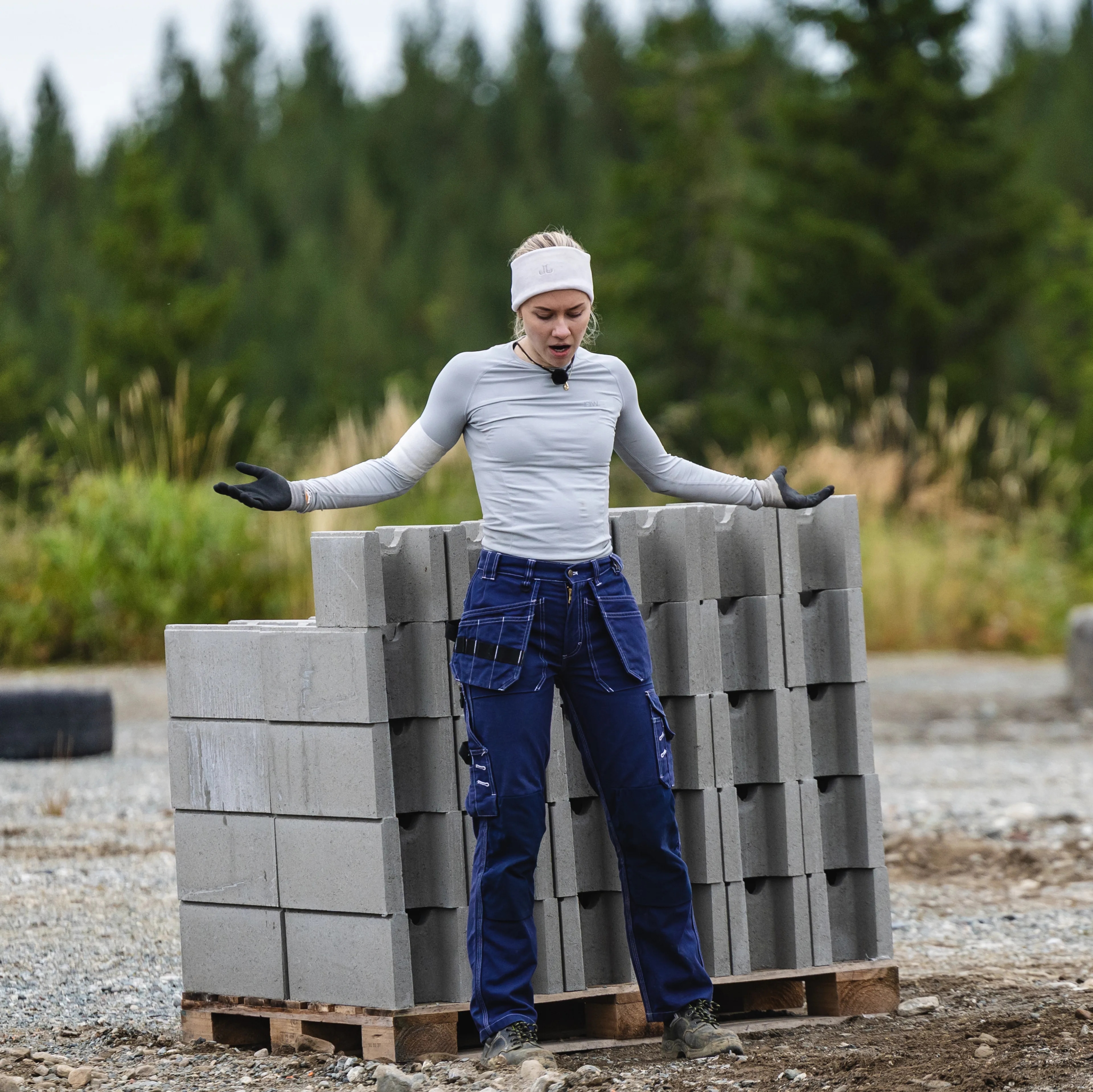 Tora står foran en pall med betongklosser. Hun er utendørs, på et gruslagt område med skog i bakgrunnen
