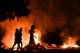YAMIL LAGE / AFP,NTB Silhuetter av personer går forbi store bål i mørket. Røyk og flammer lyser opp scenen med oransje fargetoner. En trekrone er synlig mørkt mot himmelen til venstre. (Bildebeskrivelsen er laget av en KI-tjeneste)