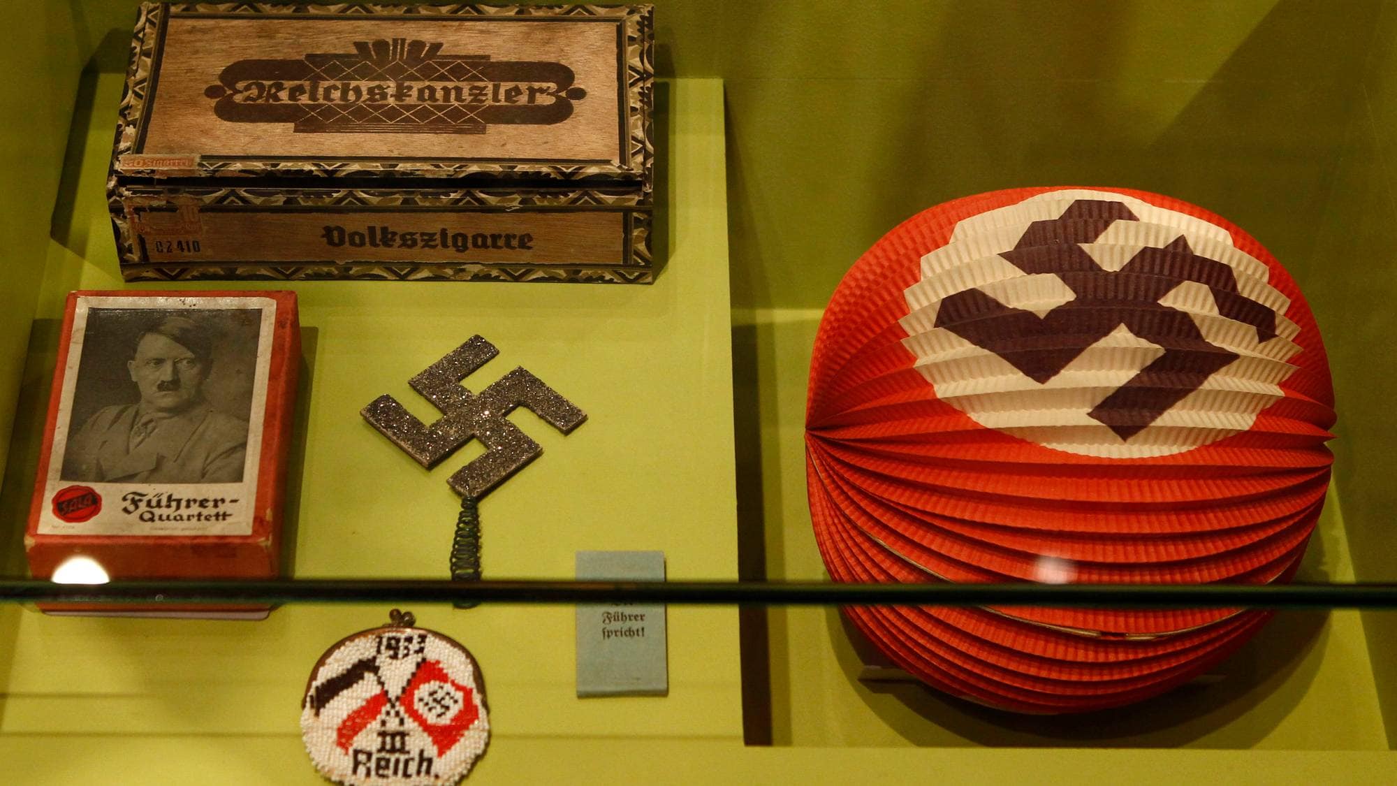 Utstilling med historiske gjenstander fra Nazi-Tyskland, inkludert en eske, et hakekors og en lykt. (Bildebeskrivelsen er laget av en KI-tjeneste)