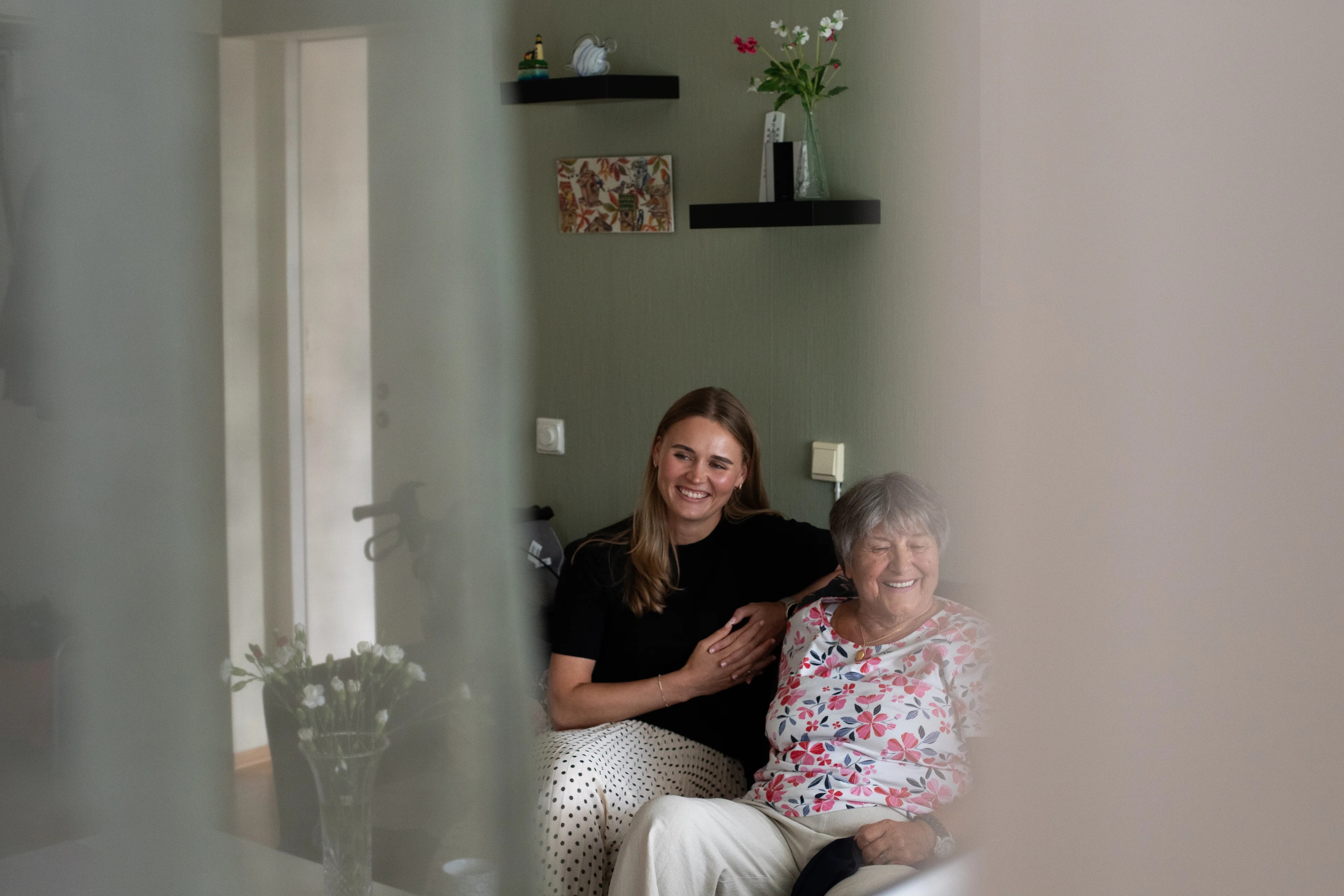 en ung kvinne som sitter ved siden av en eldre kvinne, begge ler og smiler