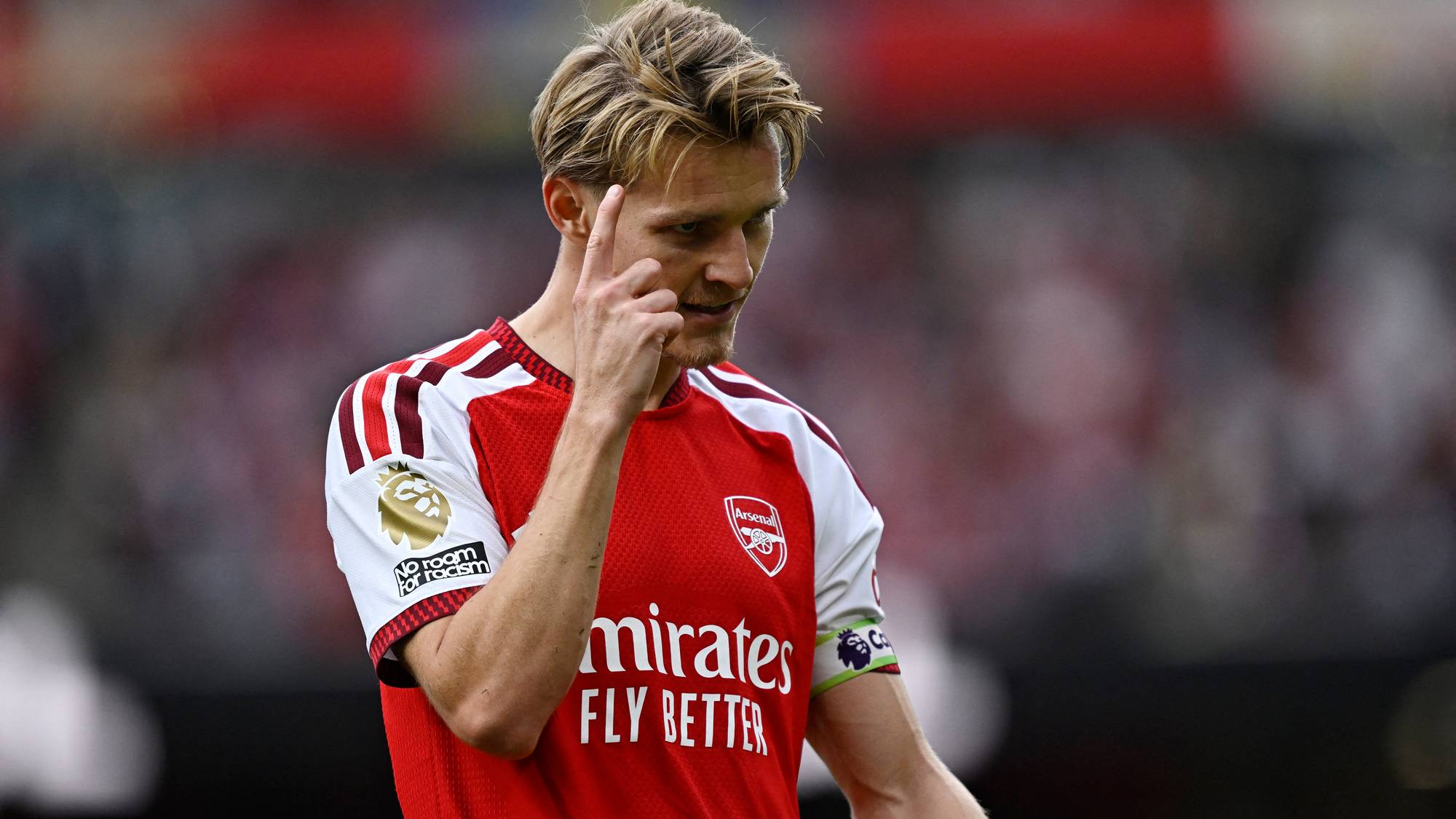 Martin Ødegaard i Arsenal-drakt peker mot hodet under en fotballkamp. (Bildebeskrivelsen er laget av en KI-tjeneste)