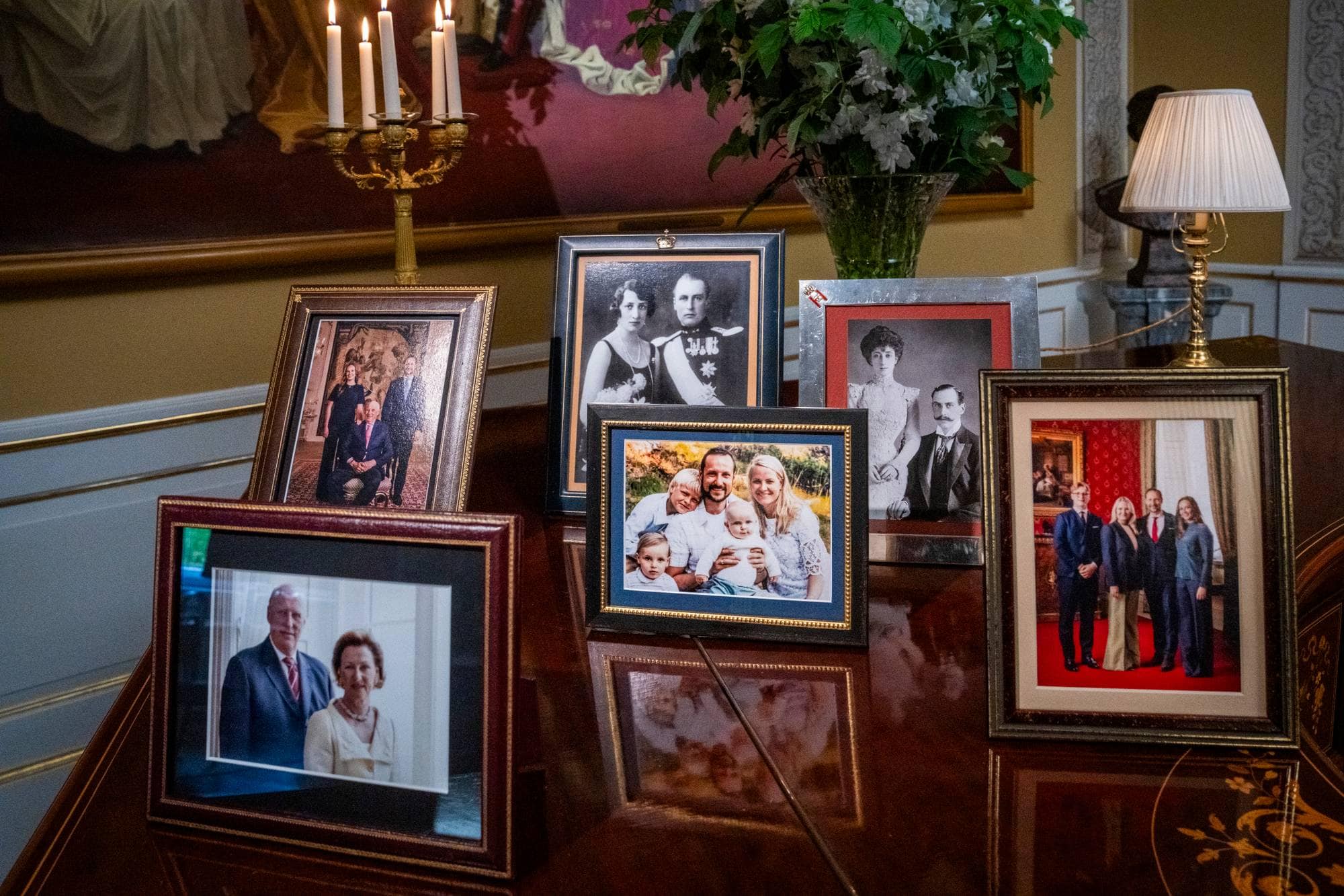 Fotografier av den norske kongefamilien utstilt på et bord i en stue. (Bildebeskrivelsen er laget av en KI-tjeneste)