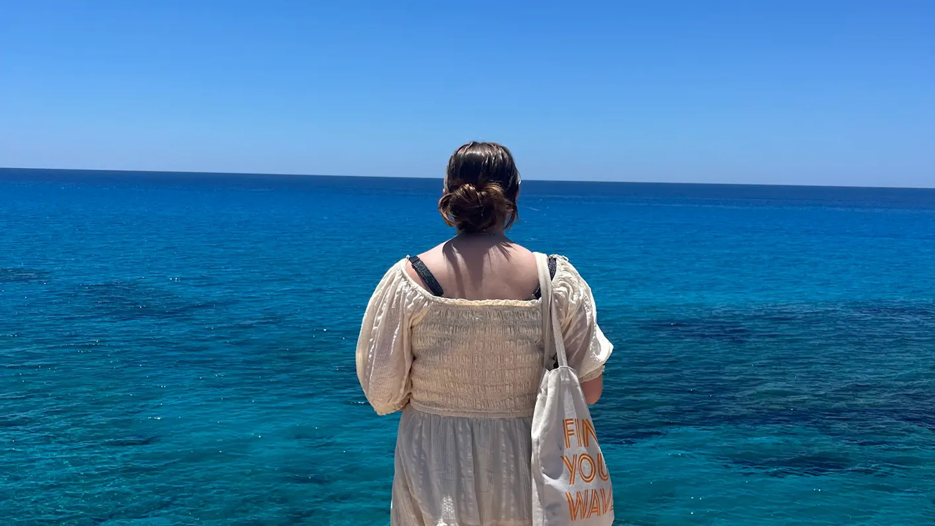 Ei jente har ryggen vendt mot kamera og ser ut mot havet