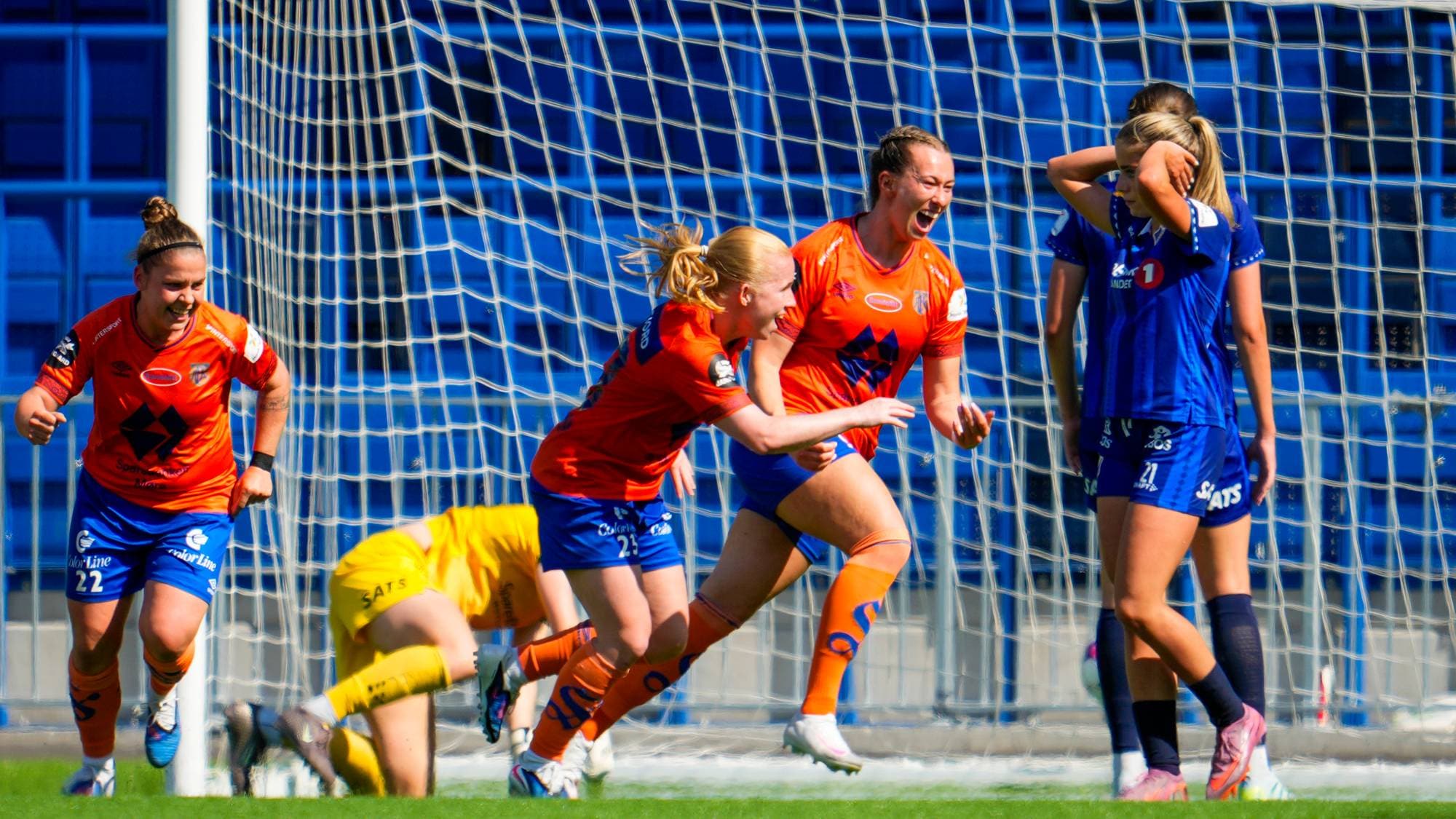 Fotballspillere i oransje jubler foran et mål, mens motstandere i blå drakter står skuffet ved siden. (Bildebeskrivelsen er laget av en KI-tjeneste)