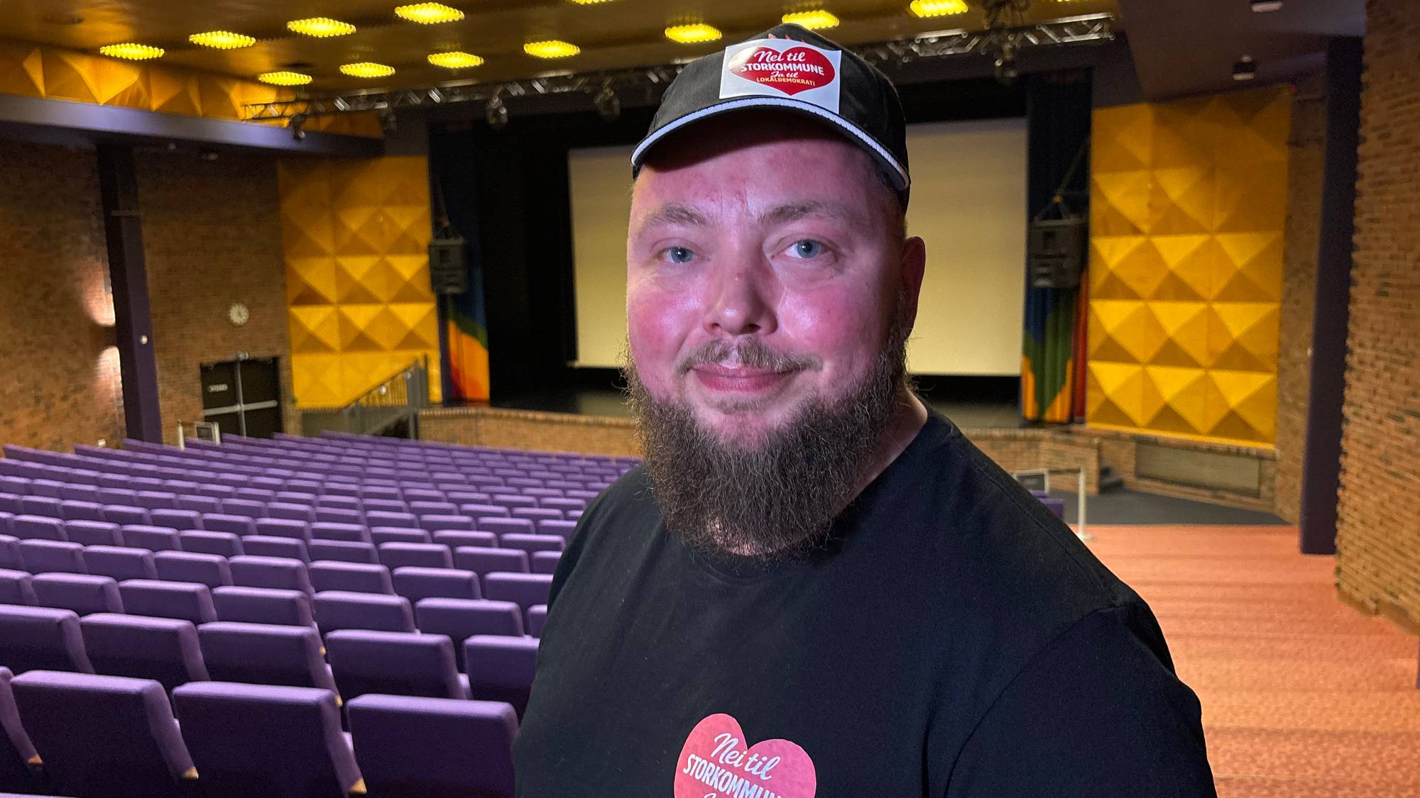 en mann i caps og sort genser med hjerte på ser i kamera