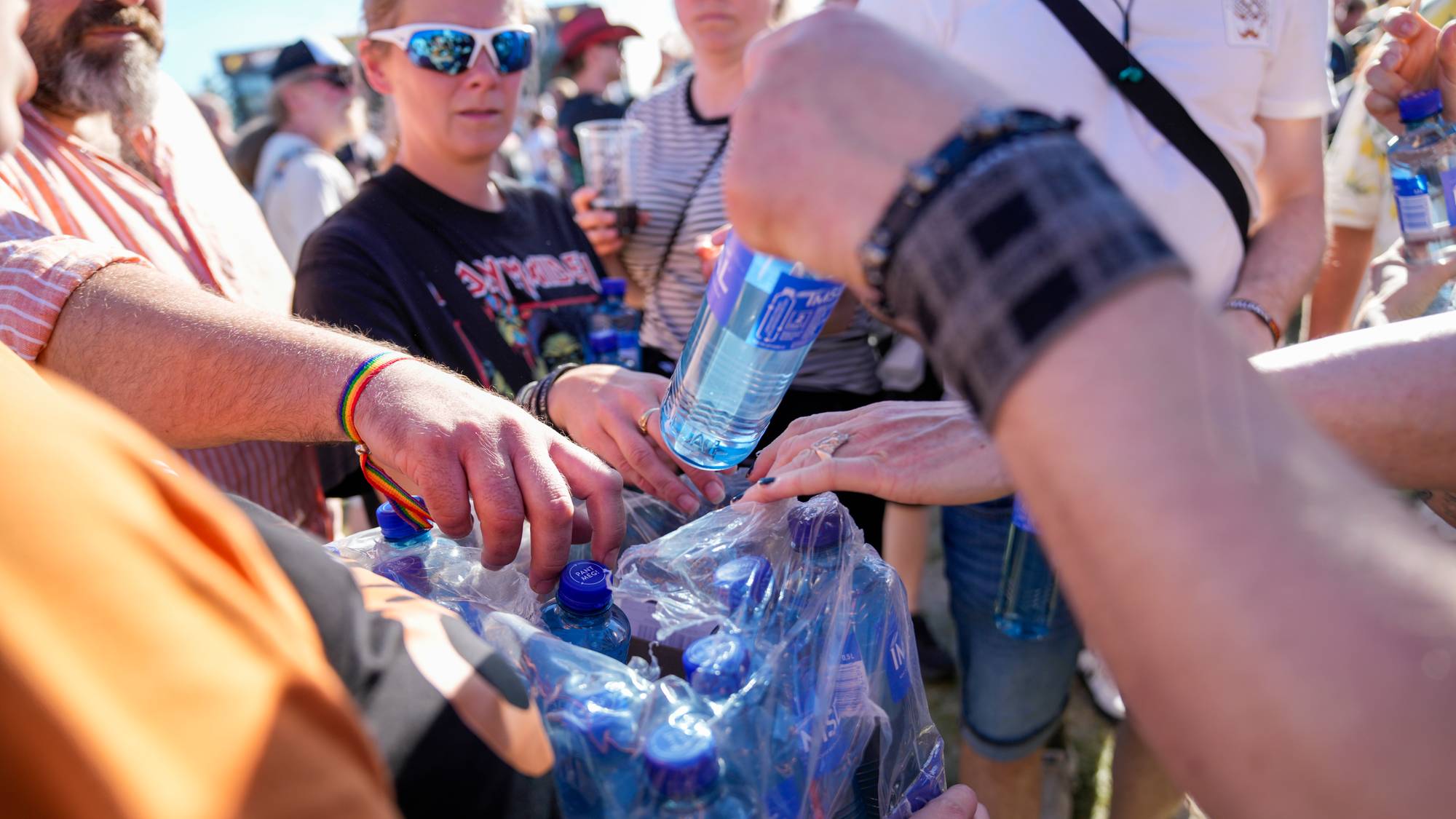 Mennesker samles om en plastpakning med vannflasker utendørs. (Bildebeskrivelsen er laget av en KI-tjeneste)