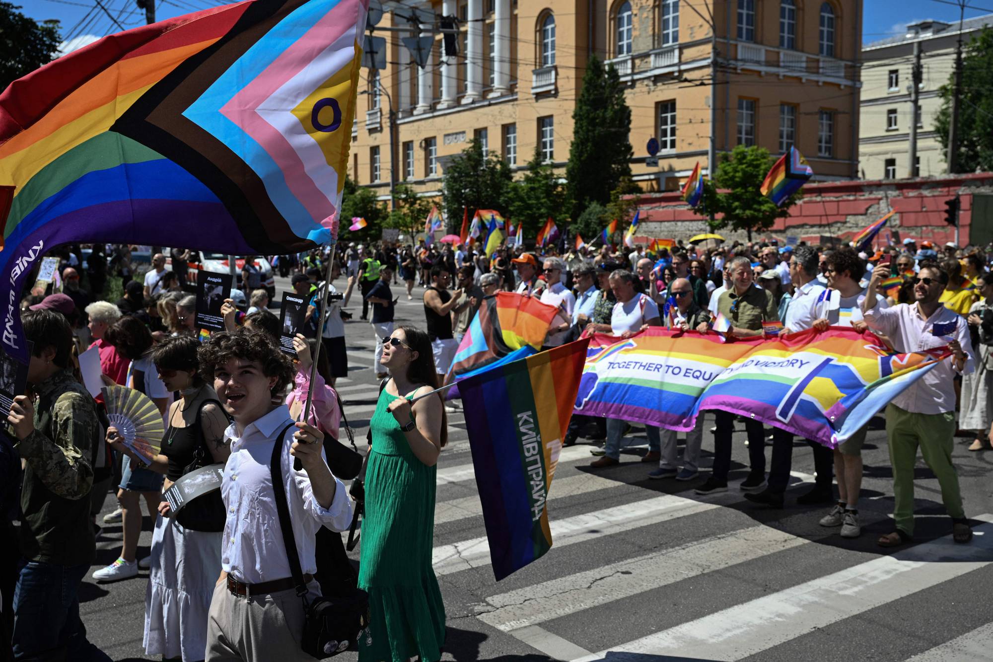 Folk går i Pride-parade i en gate i Kyiv med regnbueflagg og plakater i hendene. 