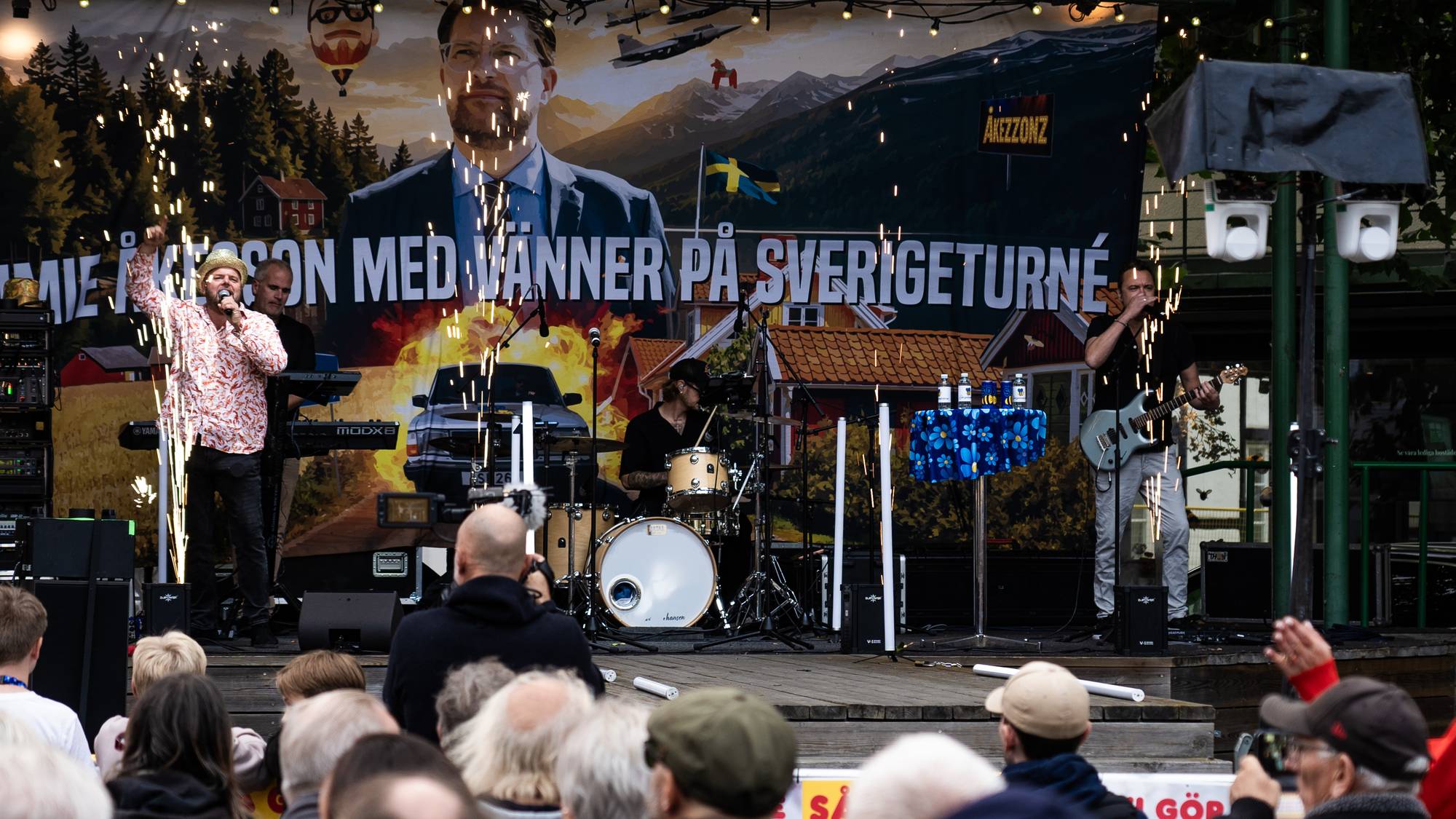 Bandet Åkezzonz spiller på en utendørs scene foran et publikum. Pyroteknikk utløses på scenen. (Bildebeskrivelsen er laget av en KI-tjeneste)