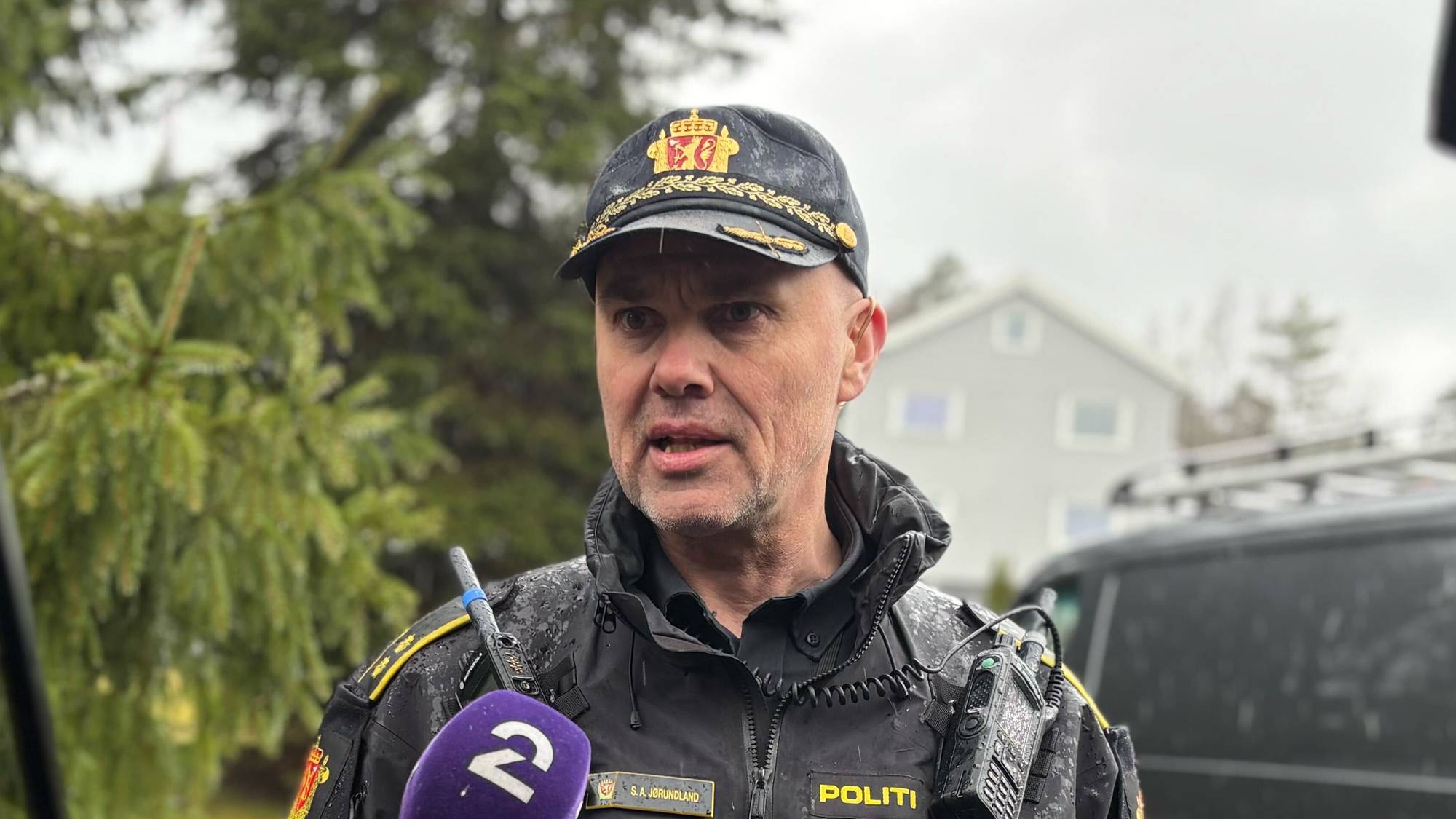 En politibetjent som står og blir intervjuet av journalister. 
