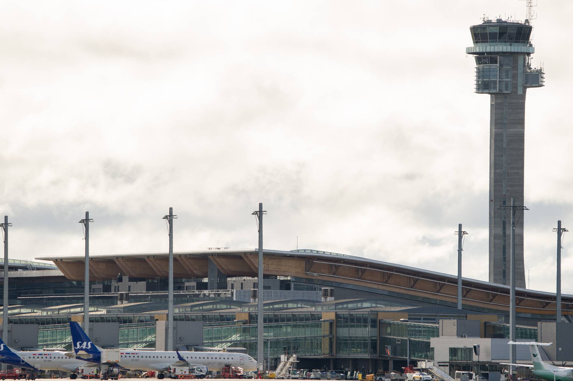 Flyplassbygning og kontrolltårn ved Oslo lufthavn med fly parkert på bakken. (Bildebeskrivelsen er laget av en KI-tjeneste)