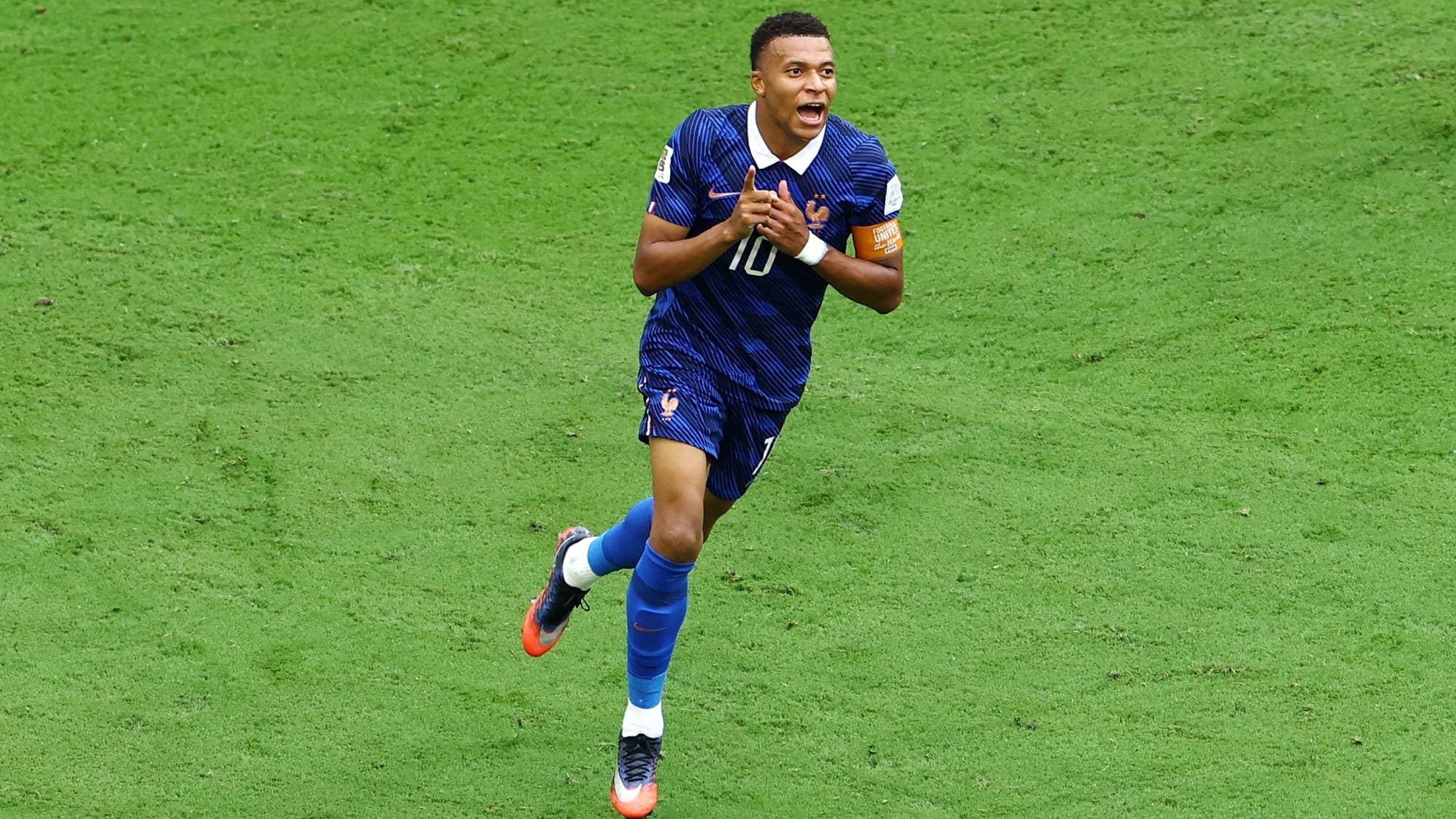 Kylian Mbappé jubler på gressbanen i Frankrikes landslagsdrakt. (Bildebeskrivelsen er laget av en KI-tjeneste)