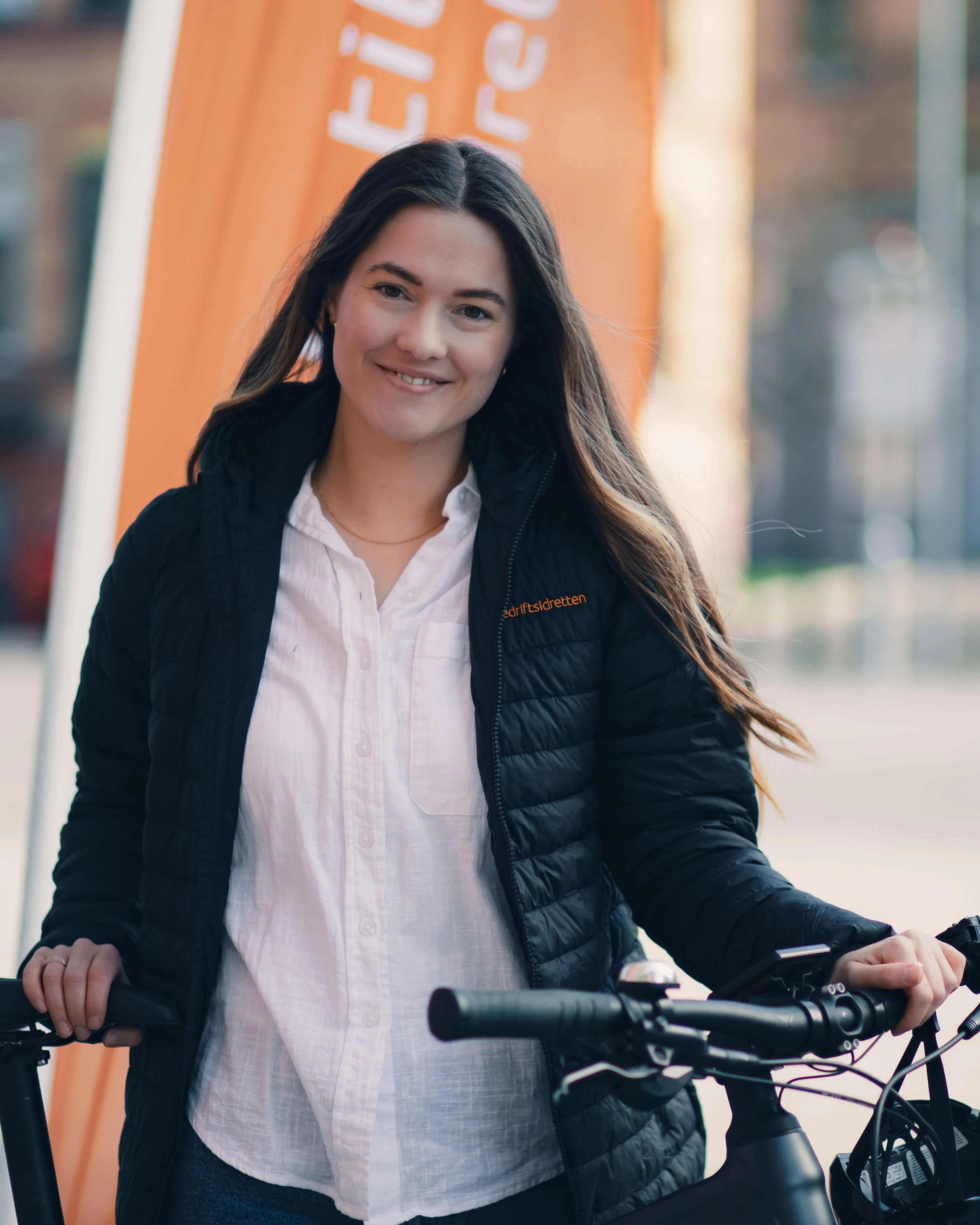 Frida Jacobsen står og holder med en sykkel mens hun smiler og ser inn i kamera.