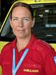 Delta En ambulanseservicemedarbeider står foran en gult ambulansekjøretøy. Hun har på seg en rød uniform med påskriften "AMBULANSE". I bakgrunnen kan deler av ambulansen sees, inkludert seter og utstyr. Det er tydelig at bildet er tatt på en ambulansestasjon. (Bildebeskrivelsen er laget av en KI-tjeneste)
