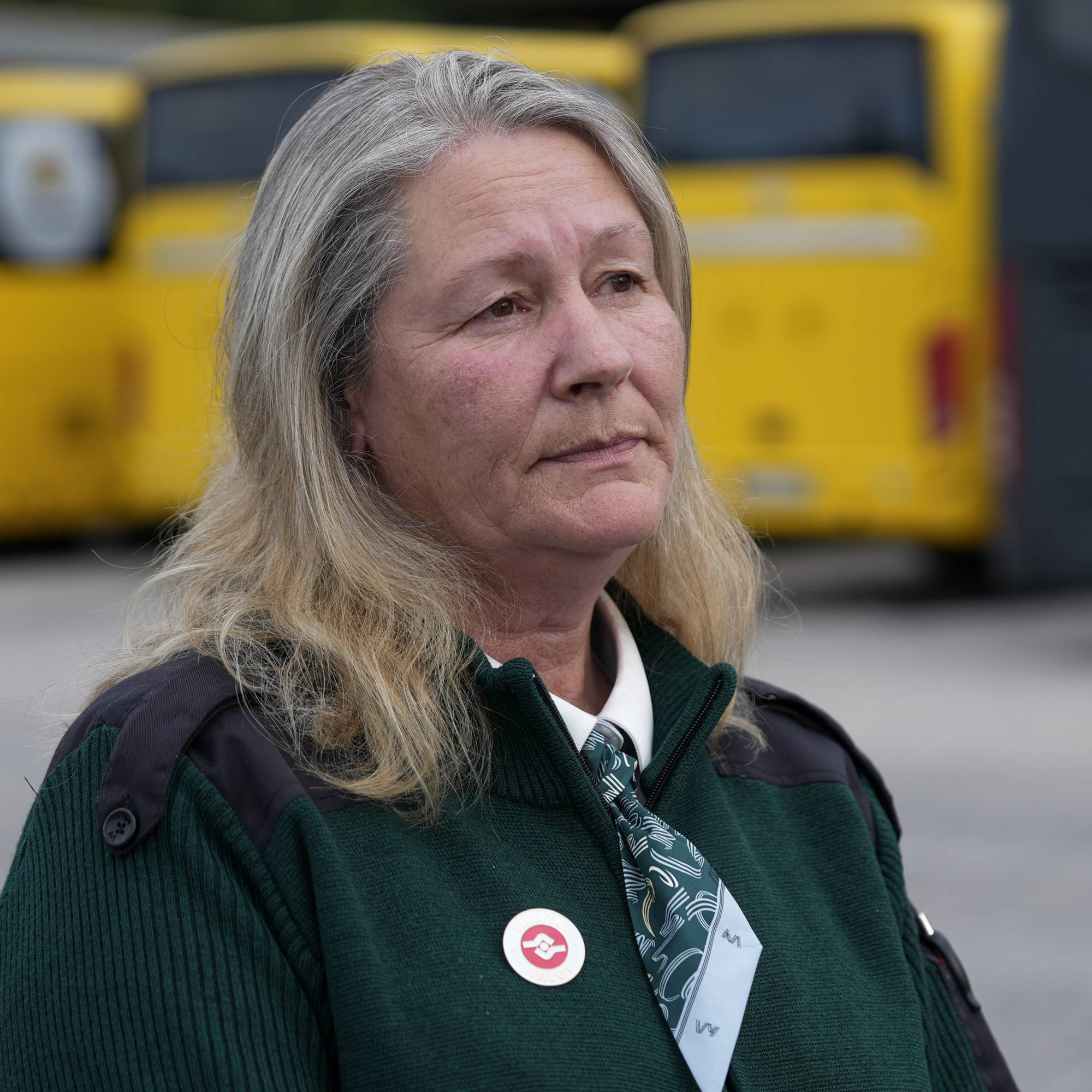 Kvinne i uniform står foran flere busser parkert på en oppstillingsplass.