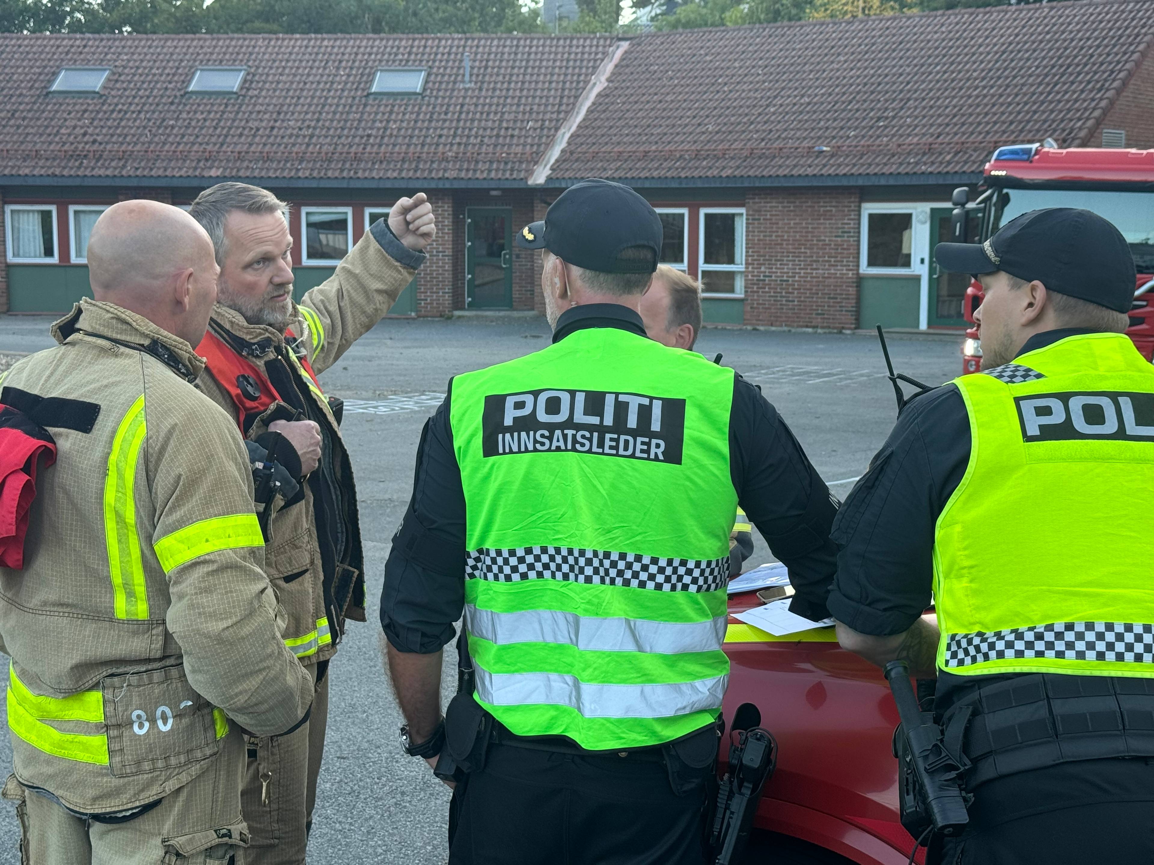 Brannmannskaper og politi i samtale foran en brannbil utenfor en bygning. (Bildebeskrivelsen er laget av en KI-tjeneste)