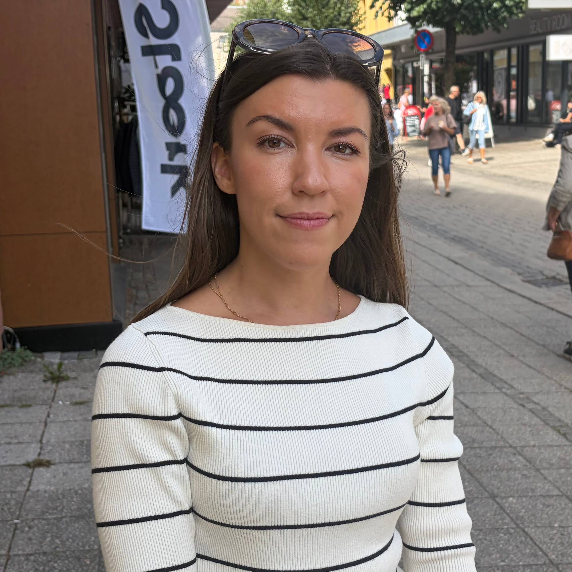 En kvinne i stripete genser står i en gågate med folk i bakgrunnen. (Bildebeskrivelsen er laget av en KI-tjeneste)
