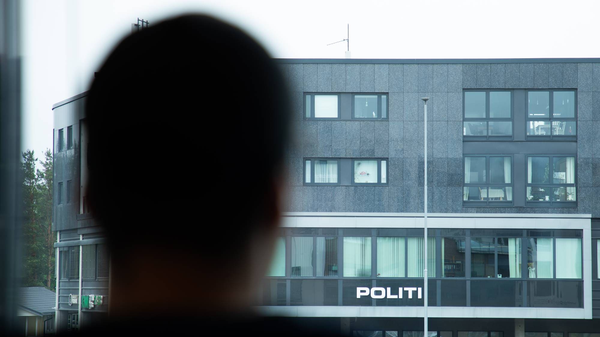 En mann står og ser ut av vinduet. På andre siden av gaten er Stjørdal politistasjon. 