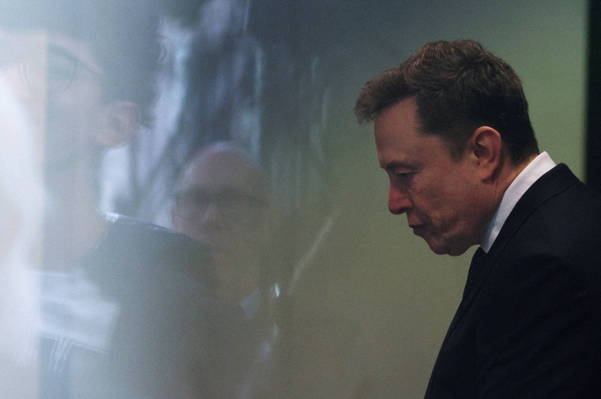 Elon Musk er sett i profil i en dress. Ved siden av ham er en NTB-logo. (Bildebeskrivelsen er laget av en KI-tjeneste)