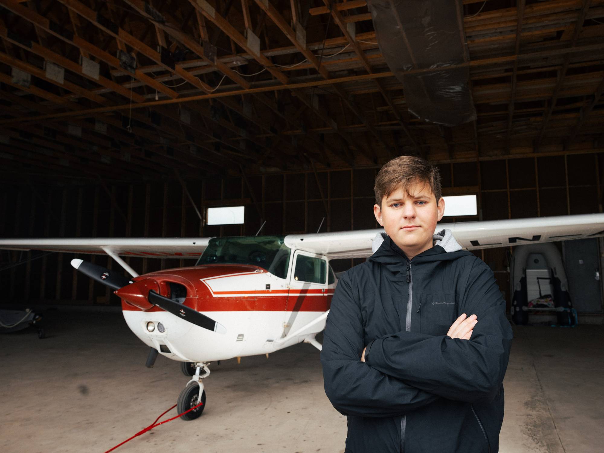 Kristoffer står foran et 37 år gammelt firemannsfly i en liten hangar. Flyet er hvitt og rødt. Han har armene i kryss og ser lurt inn i kamera.