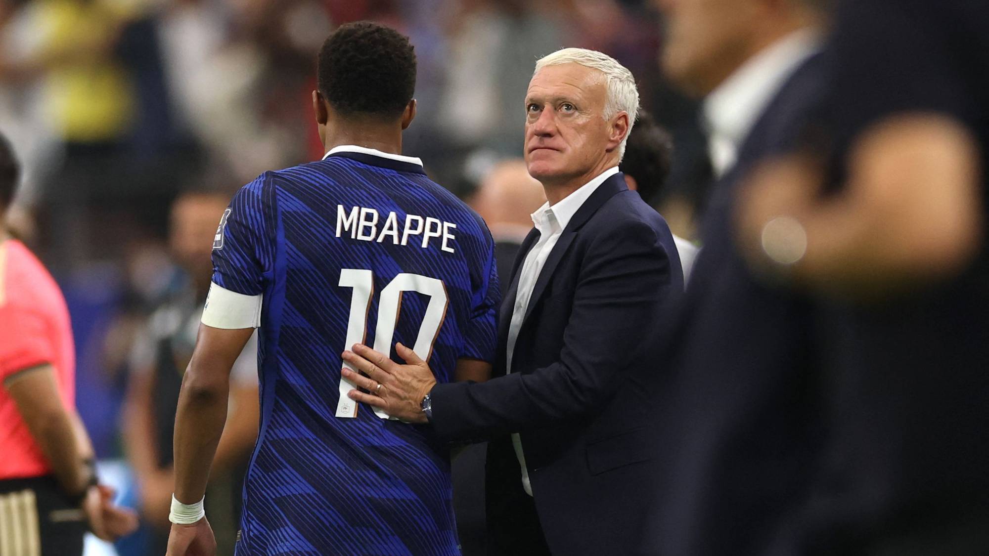 Kylian Mbappé med landslagstrener Didier Deschamps på fotballbane. (Bildebeskrivelsen er laget av en KI-tjeneste)