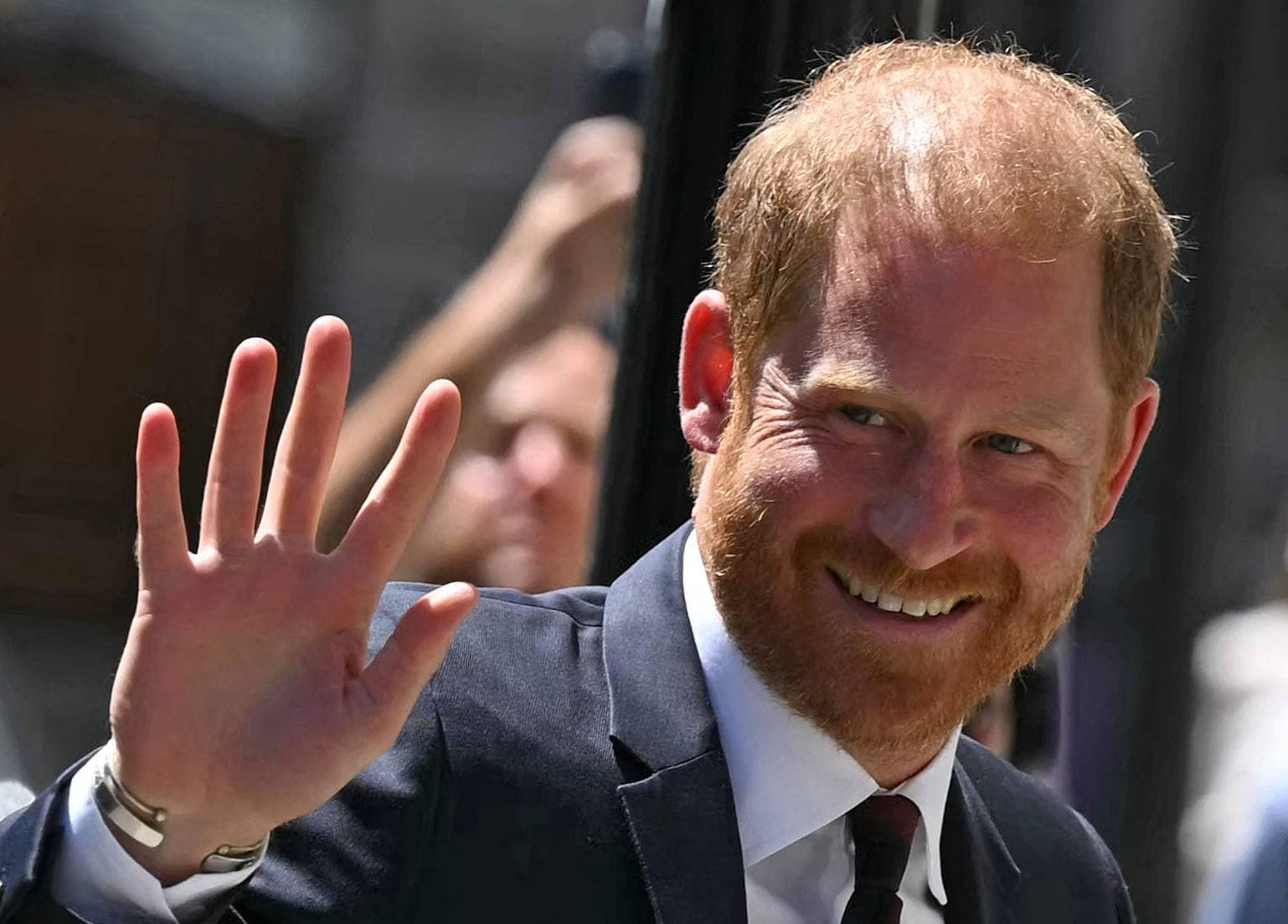 Prins Harry smiler og vinker til folkemengden. Han er kledd i en mørk dress. (Bildebeskrivelsen er laget av en KI-tjeneste)