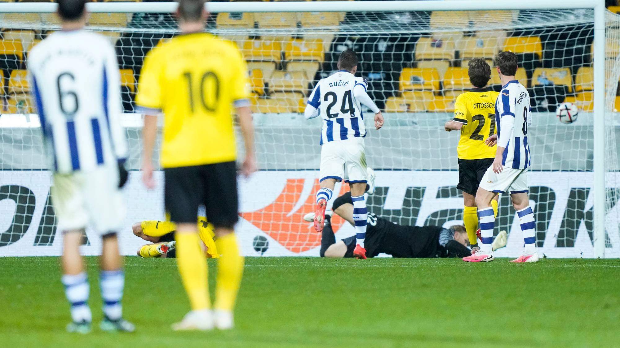 Fotballspillere i blåhvite og gule drakter foran et mål på en fotballstadion. (Bildebeskrivelsen er laget av en KI-tjeneste)