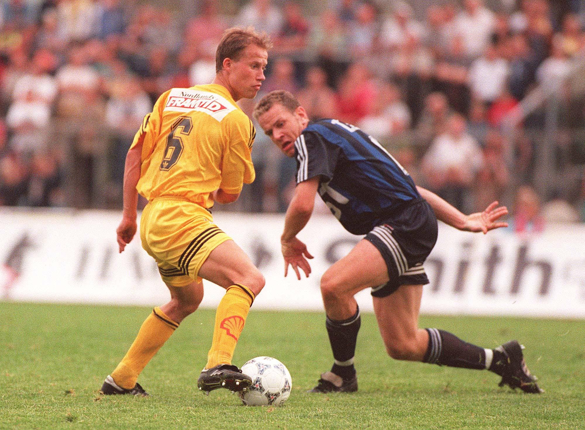 To fotballspillere kjemper om ballen på en gressbane foran et publikum. (Bildebeskrivelsen er laget av en KI-tjeneste)