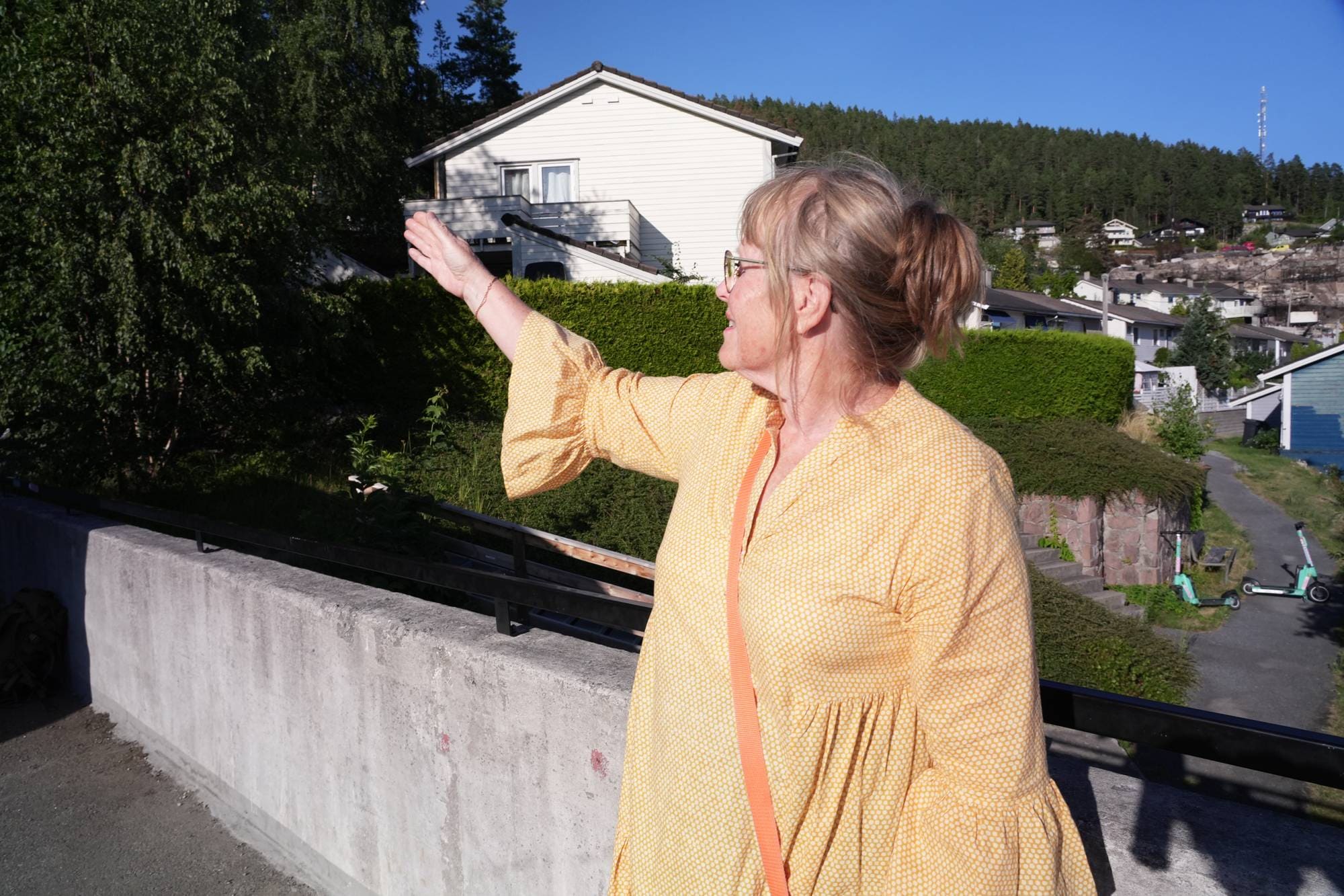 Kvinne i gul kjole peker mot et hus i et boligområde. (Bildebeskrivelsen er laget av en KI-tjeneste)