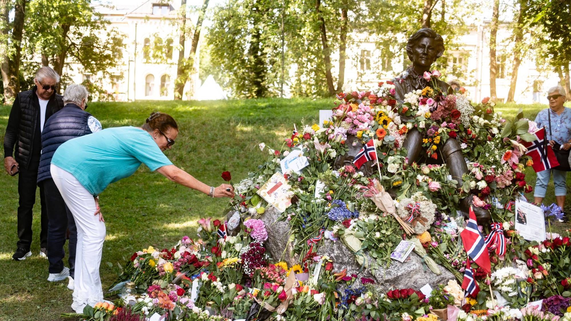 Person legger ned rose ved blomsterhavet rundt Gro Harlem Brundtland-statuen i en park. (Bildebeskrivelsen er laget av en KI-tjeneste)