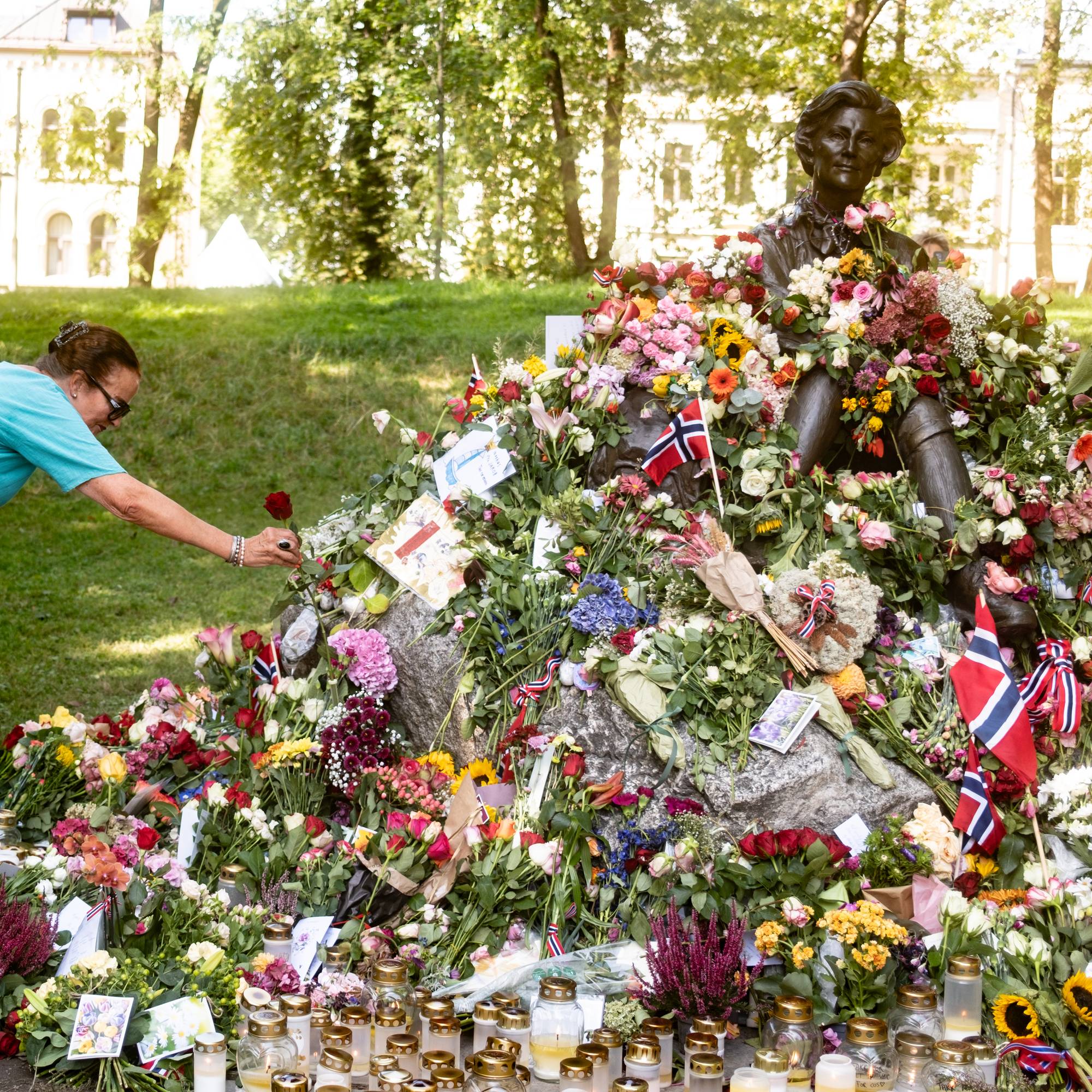 Person legger ned rose ved blomsterhavet rundt Gro Harlem Brundtland-statuen i en park. (Bildebeskrivelsen er laget av en KI-tjeneste)