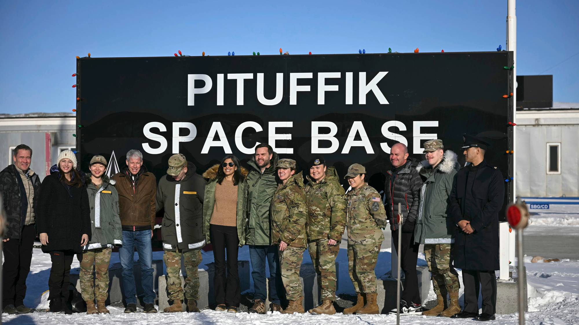 En gruppe mennesker står foran et skilt merket Pituffik Space Base i et snødekket landskap. (Bildebeskrivelsen er laget av en KI-tjeneste)