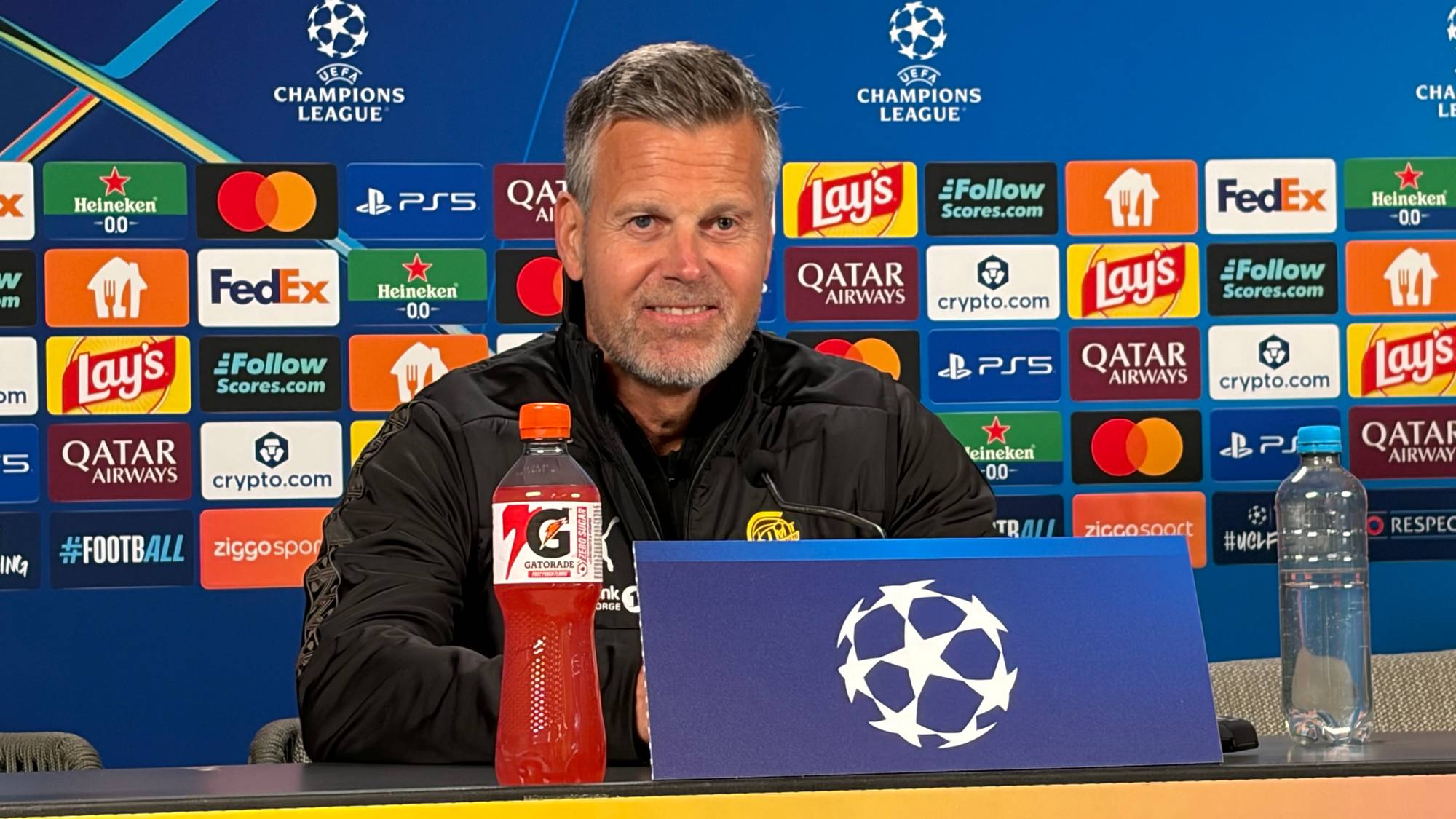Trener Kjetil Knutsen sitter på pressekonferanse foran en Champions League-vegg. (Bildebeskrivelsen er laget av en KI-tjeneste)
