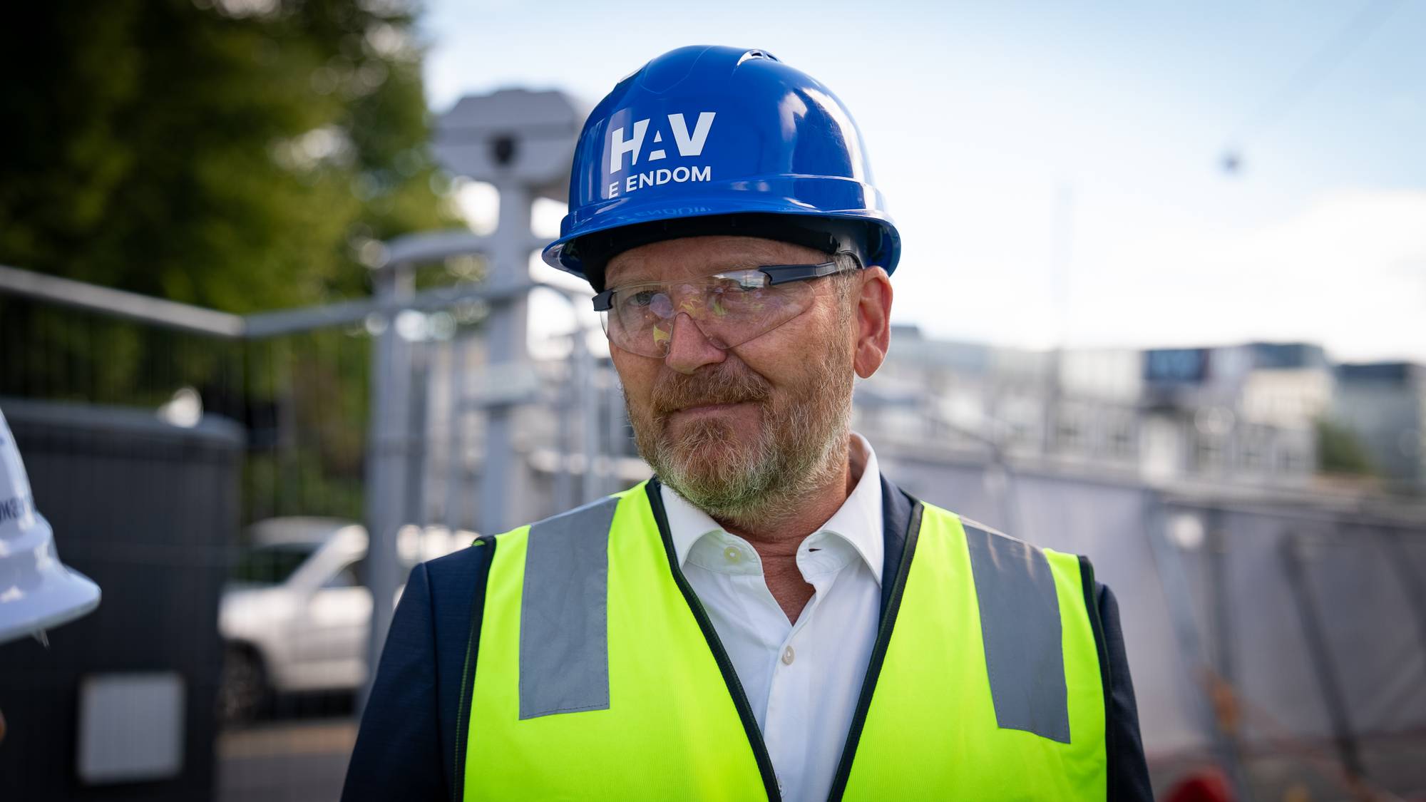 Mann i gul refleksvest, vernebriller og blå hjelm med teksten HAV E ENDOM utendørs. 