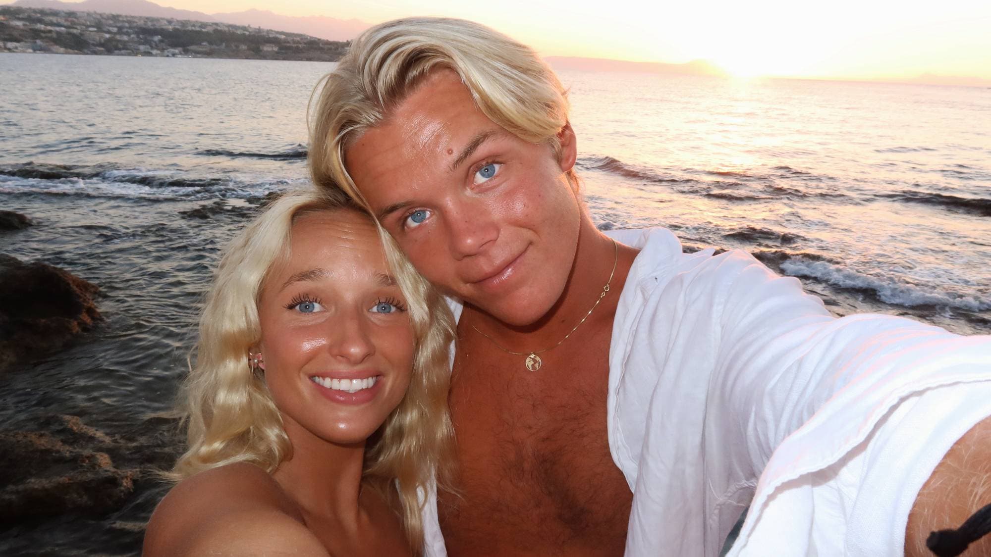 Selfie av Lea Steen Klæboe og Alex Noddeland tatt i solnedgang på en strand med havet i bakgrunnen